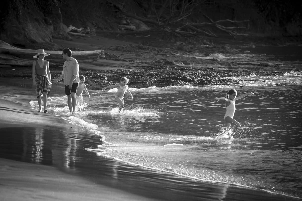 A couple walking on the beach while their kids play in the water.