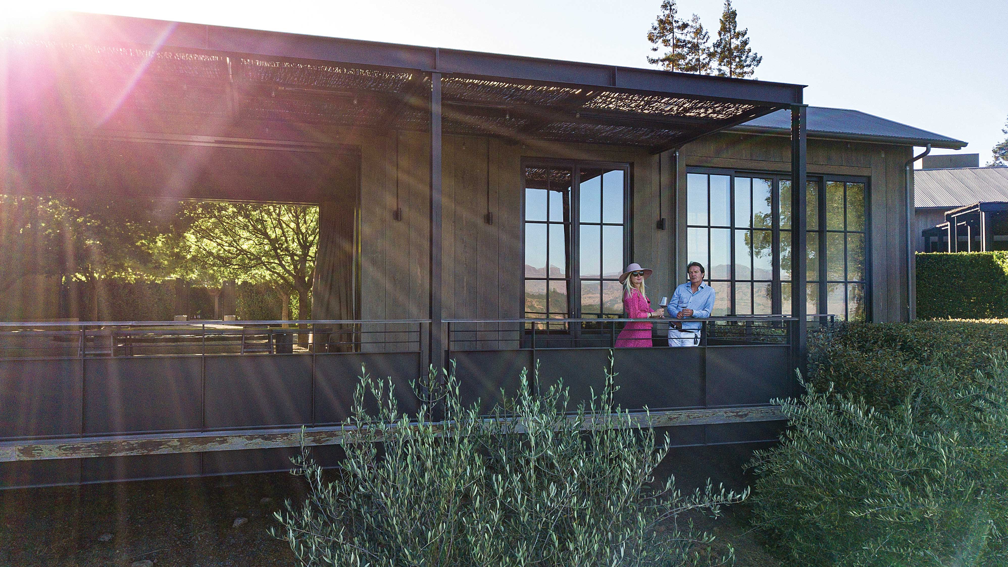 Two people wine tasting on the sunny deck of Promontory Winery, surrounded by the natural beauty of verdant trees and shrubs