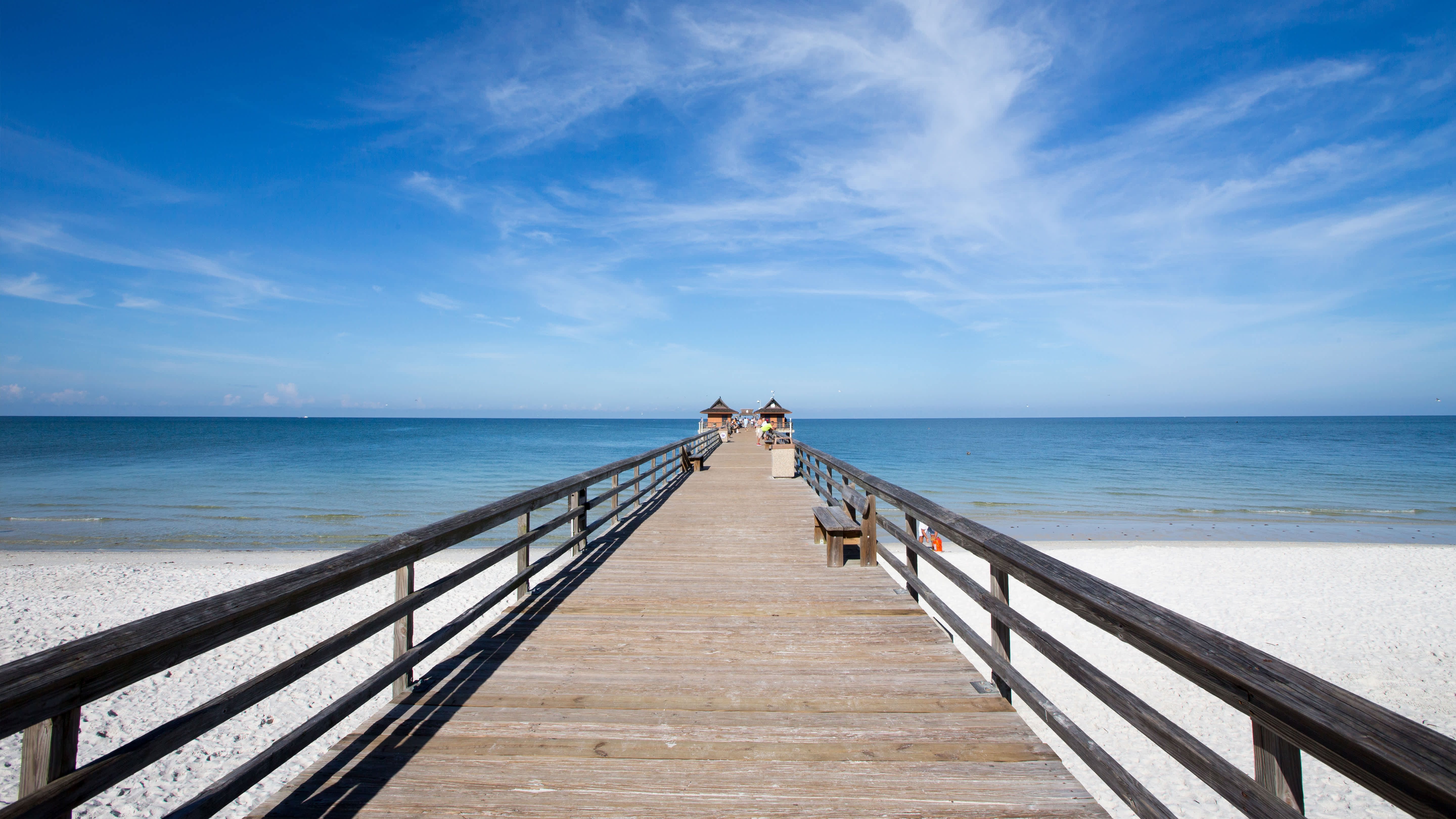 Wooden pier leading to thatched gazebos over water, close to Exclusive Resorts properties in Naples, Florida.
