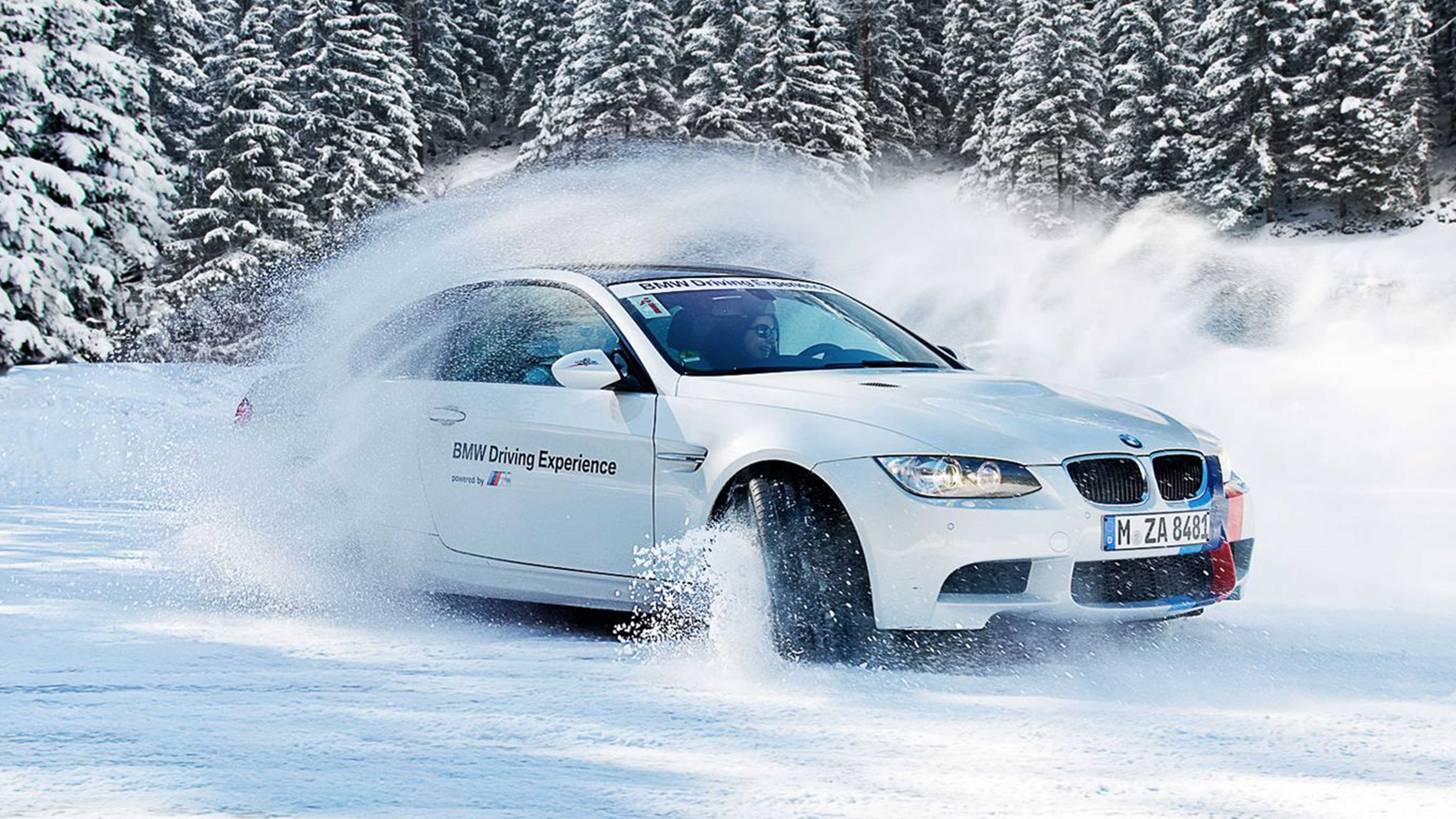 White BMW driving through a snowy landscape with snow-covered trees in the background.