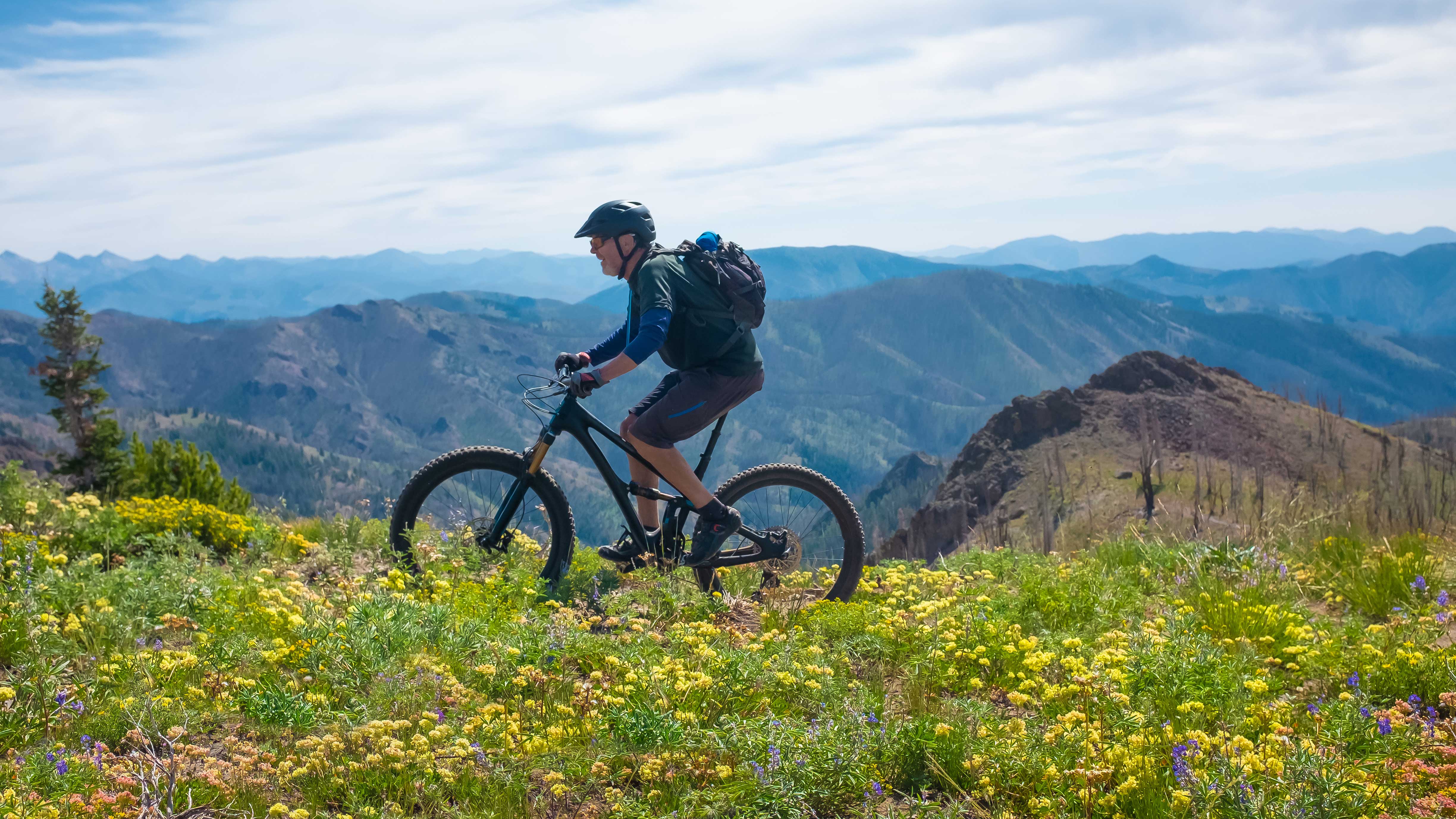 Mountain biker enjoying a ride amidst colorful wildflowers with panoramic mountain views in Sun Valley, Idaho.
