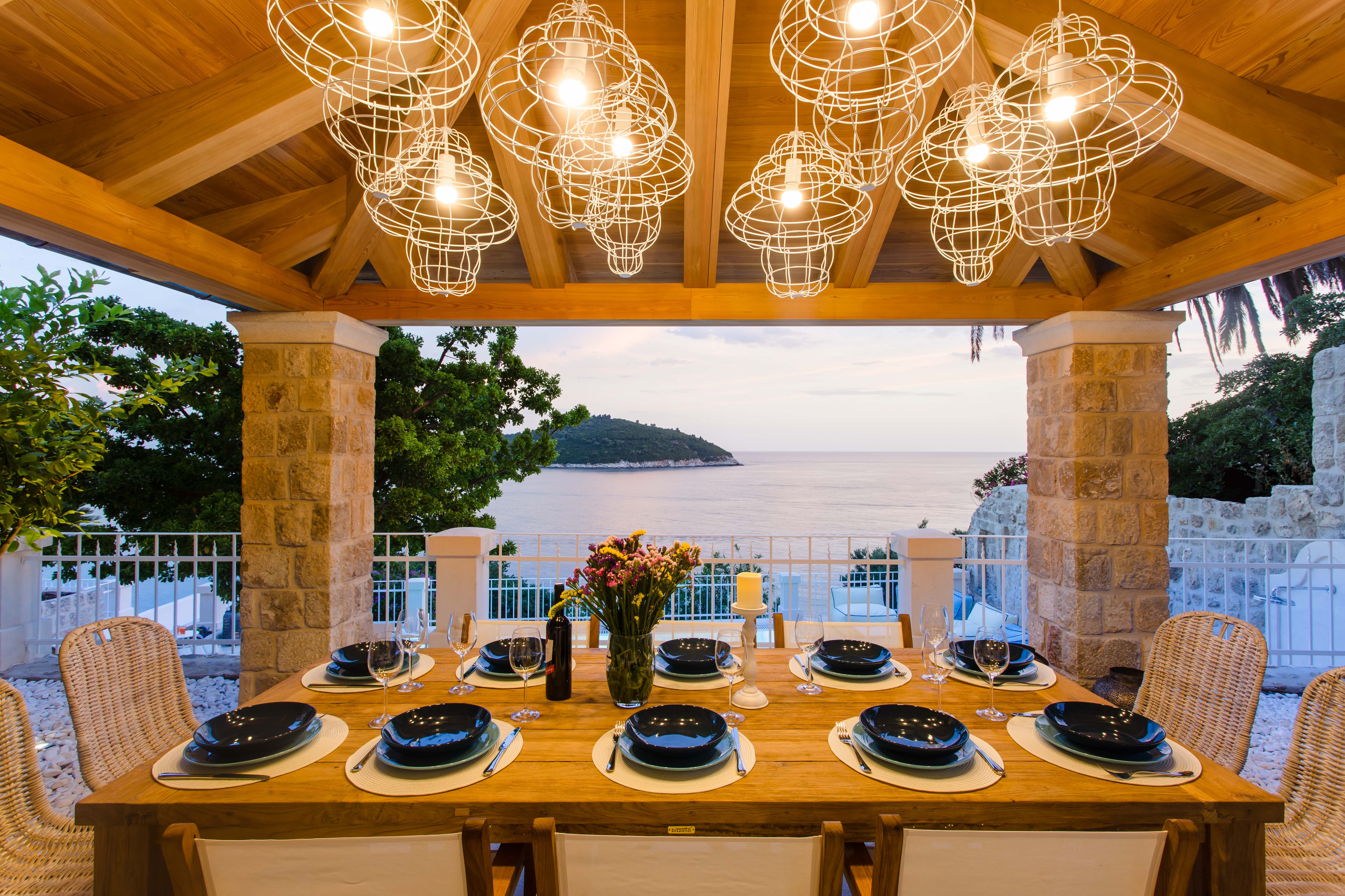 Exclusive Resorts' outdoor dining area in Dubrovnik, Croatia, with elegant lighting, a wooden table set for dinner, and views of the Adriatic Sea.