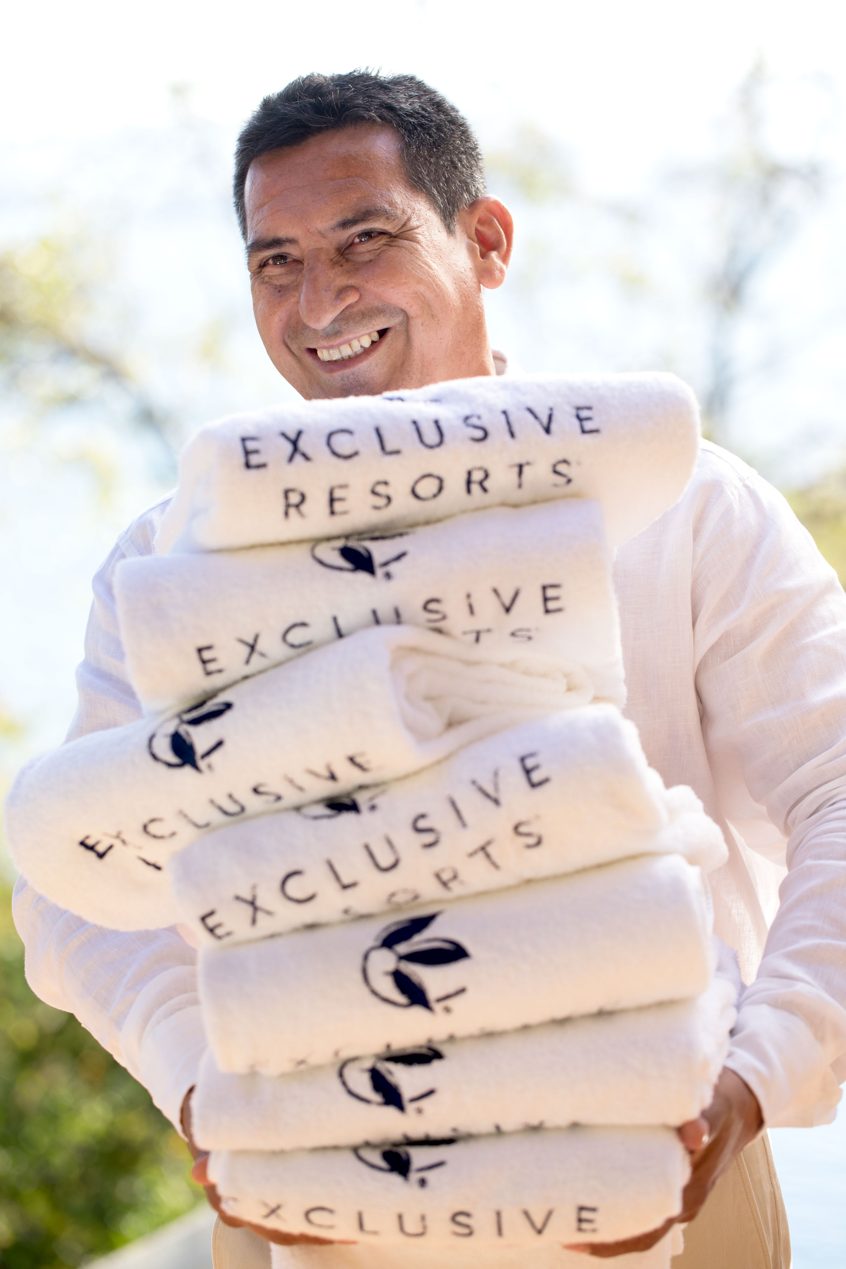 An on-site concierge at an Exclusive Resorts private home holding a stack of branded towels.