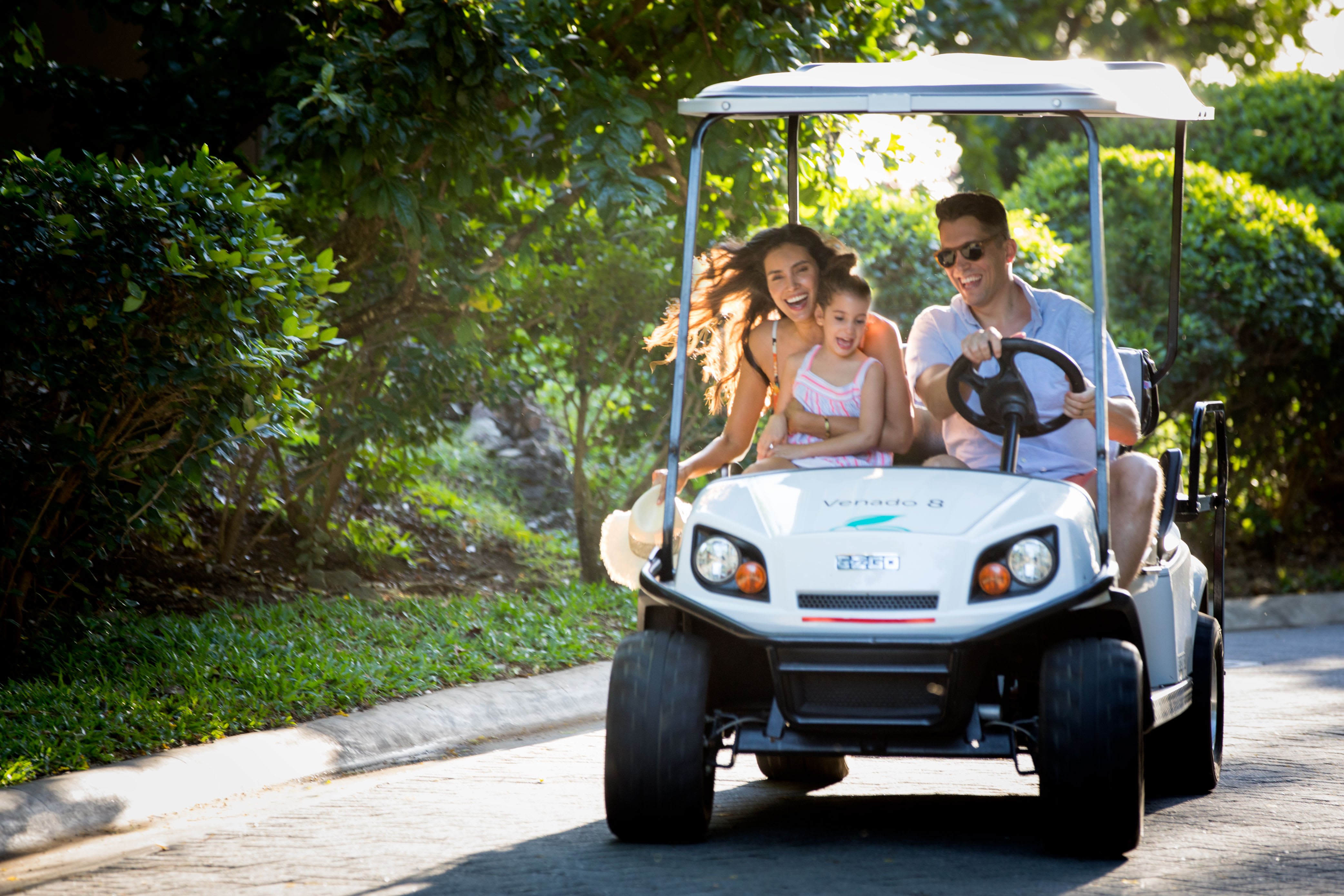 Young family laughing and riding in a golf cart.