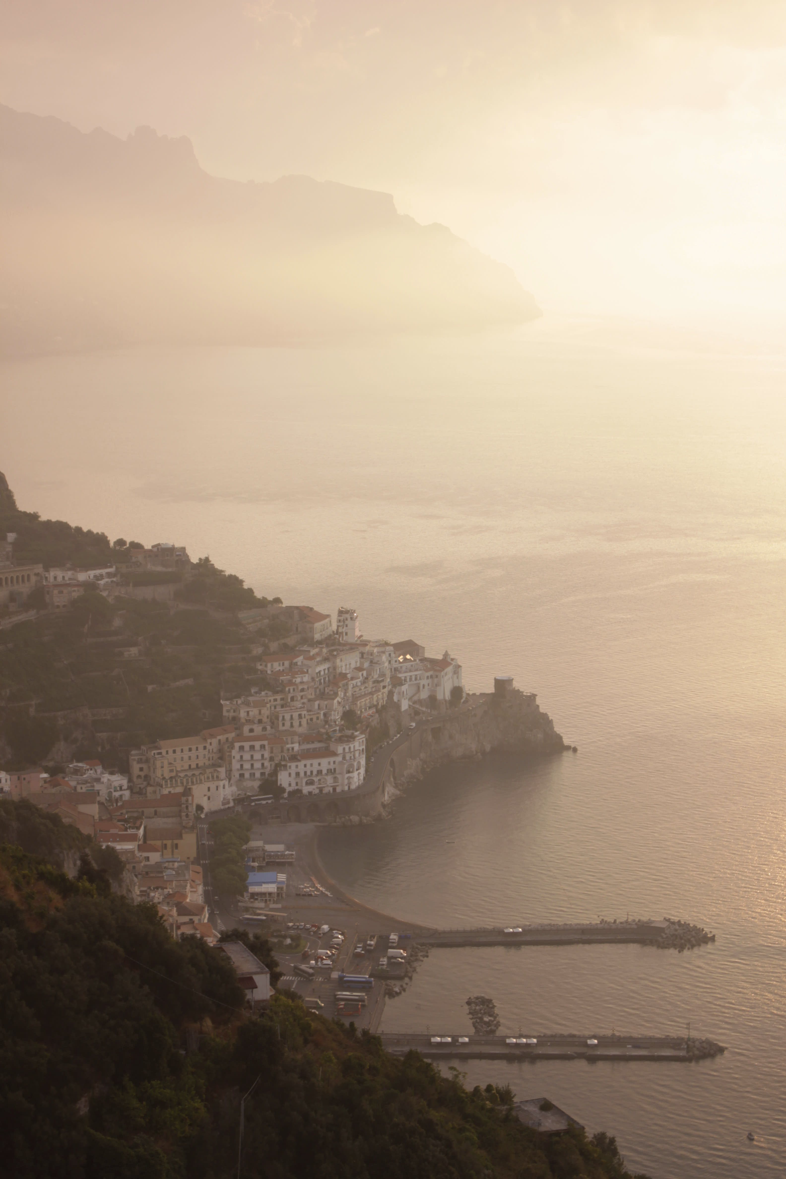 Amalfi Coast town bathed in golden sunset light with mist over the sea.