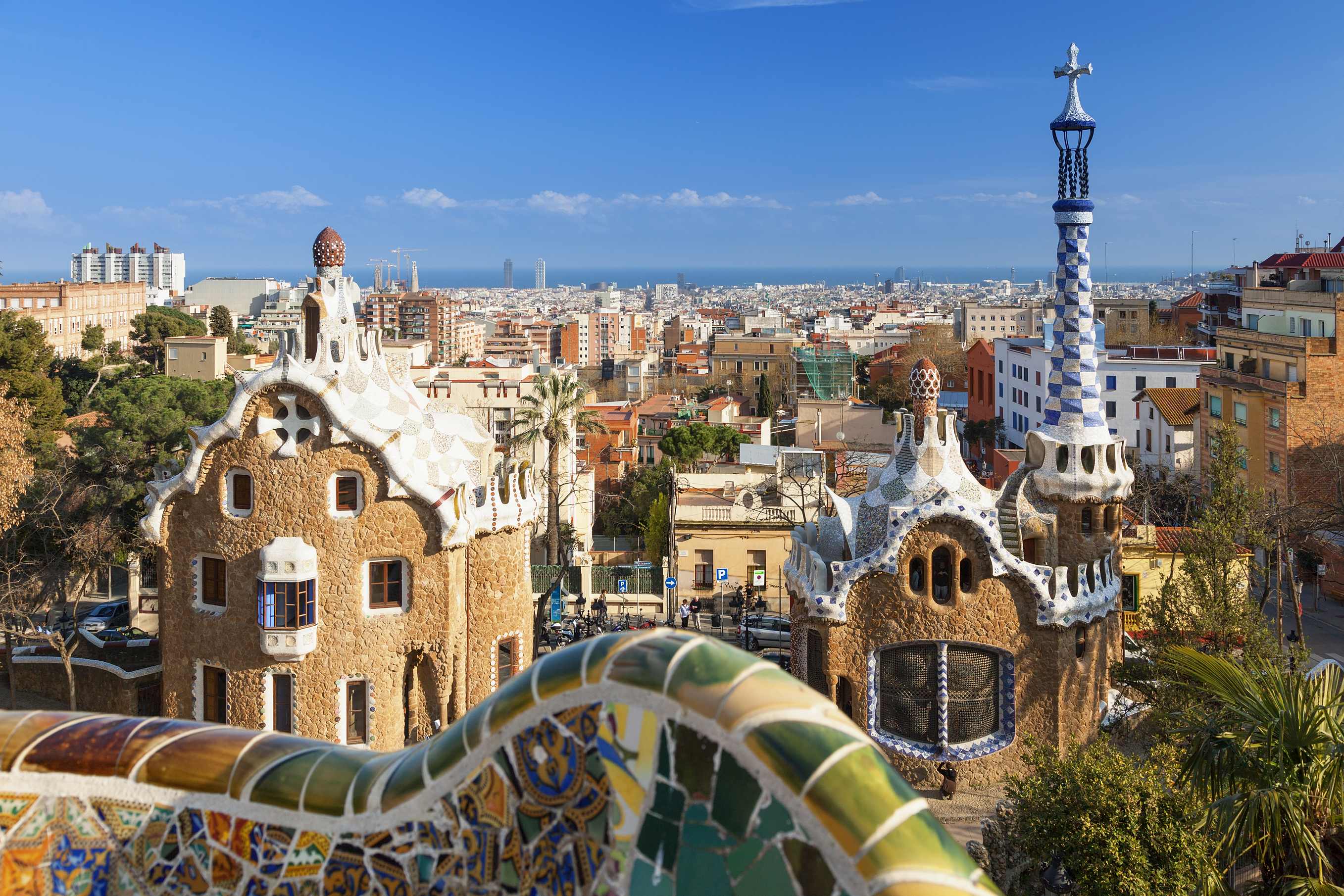 Gaudí's Park Güell in Barcelona, with its distinctive architectural elements and mosaic details, overlooking the cityscape with clear blue skies.