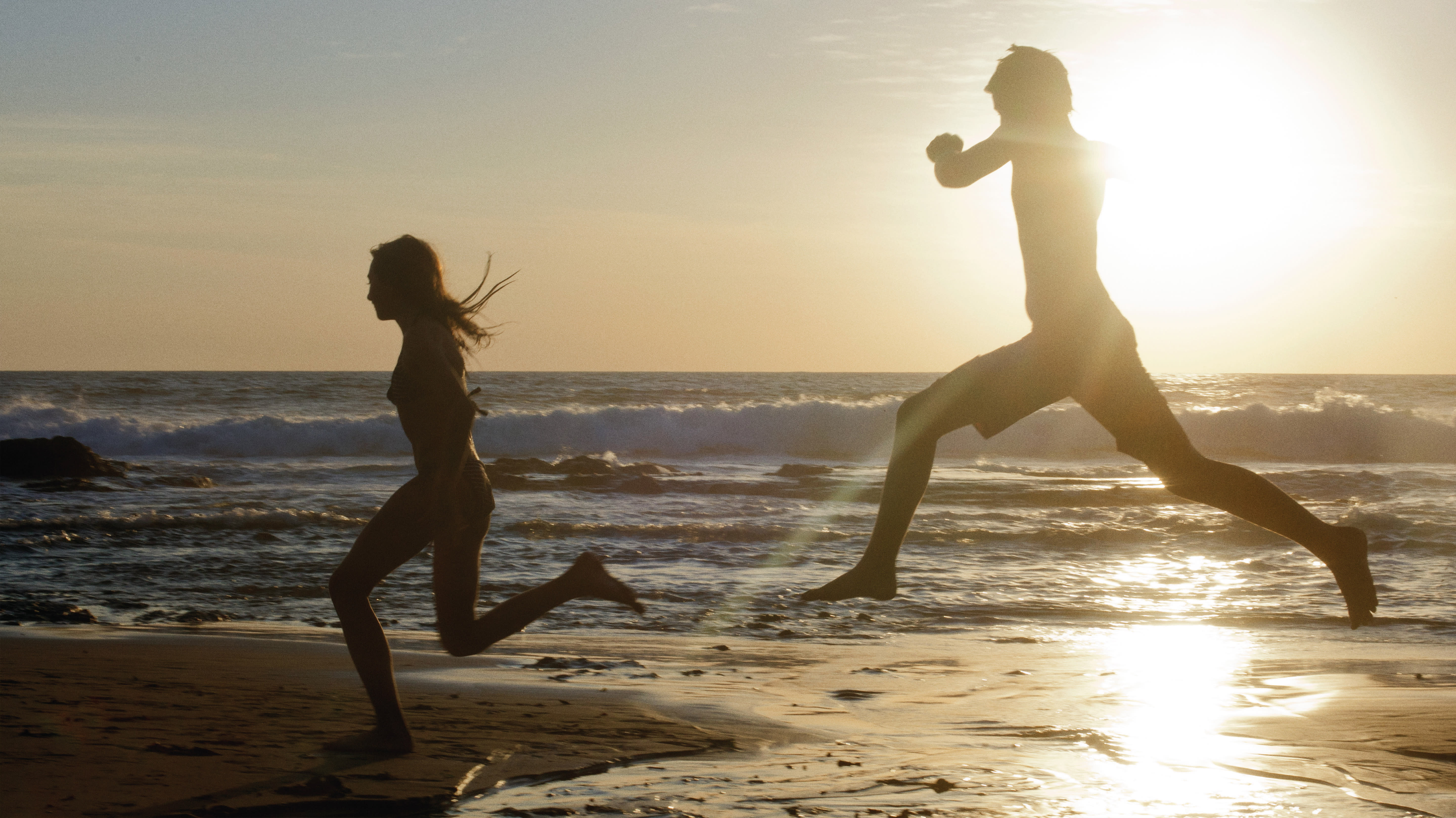 Two people running across a beach.