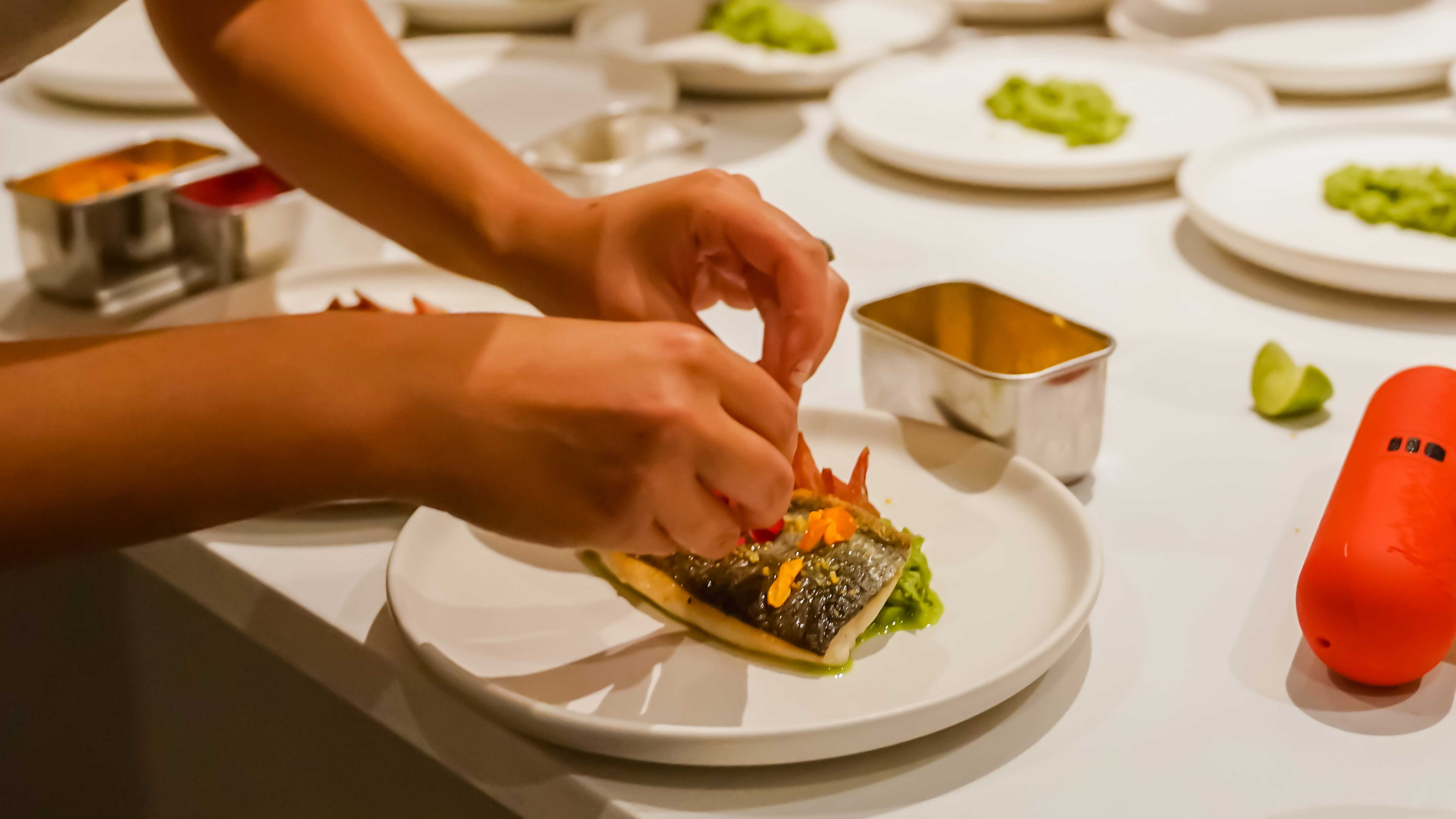Chef carefully plating a gourmet fish dish in a restaurant kitchen.