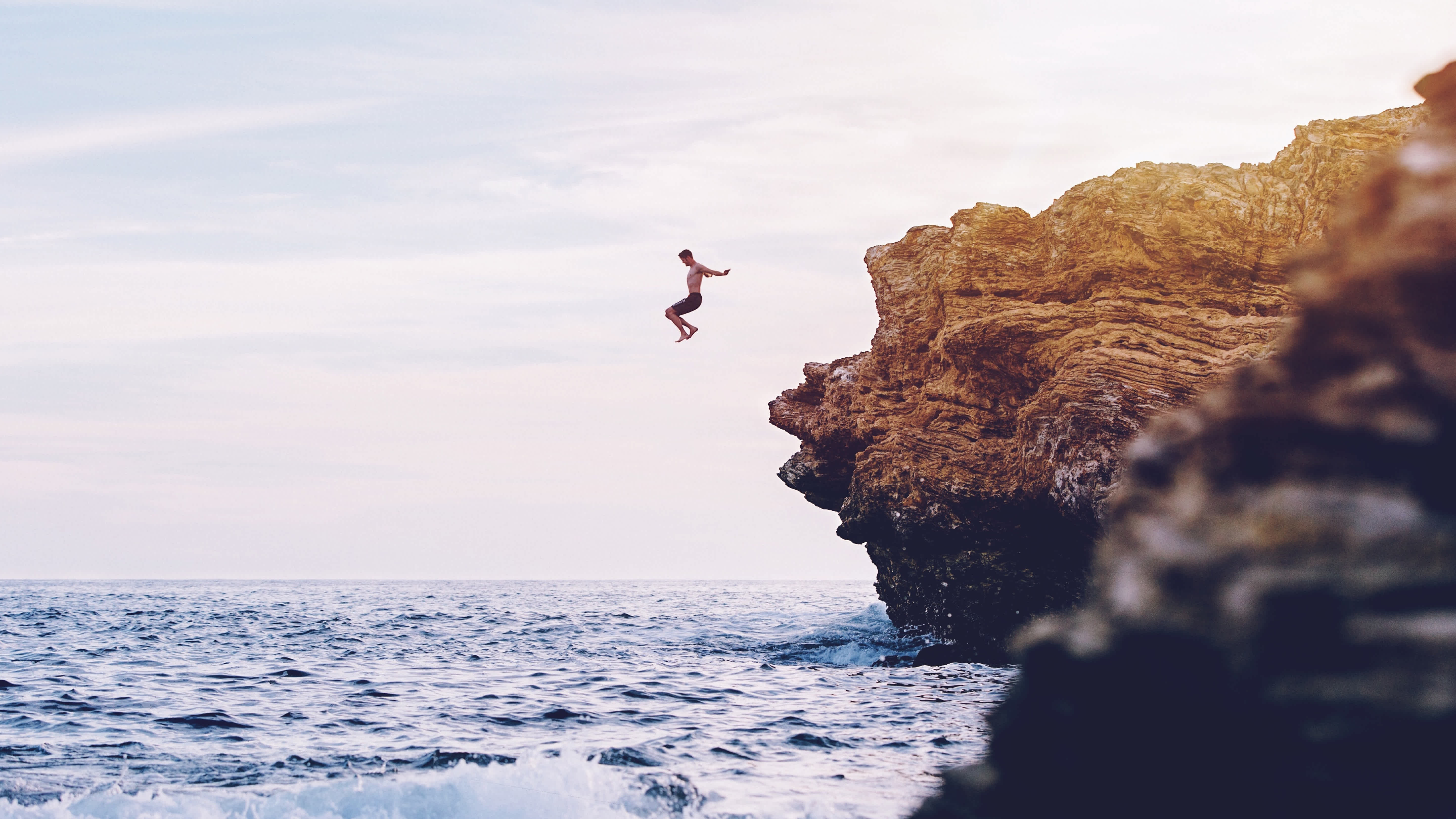 A person cliff-jumping into the water at sunset in Newport, California.