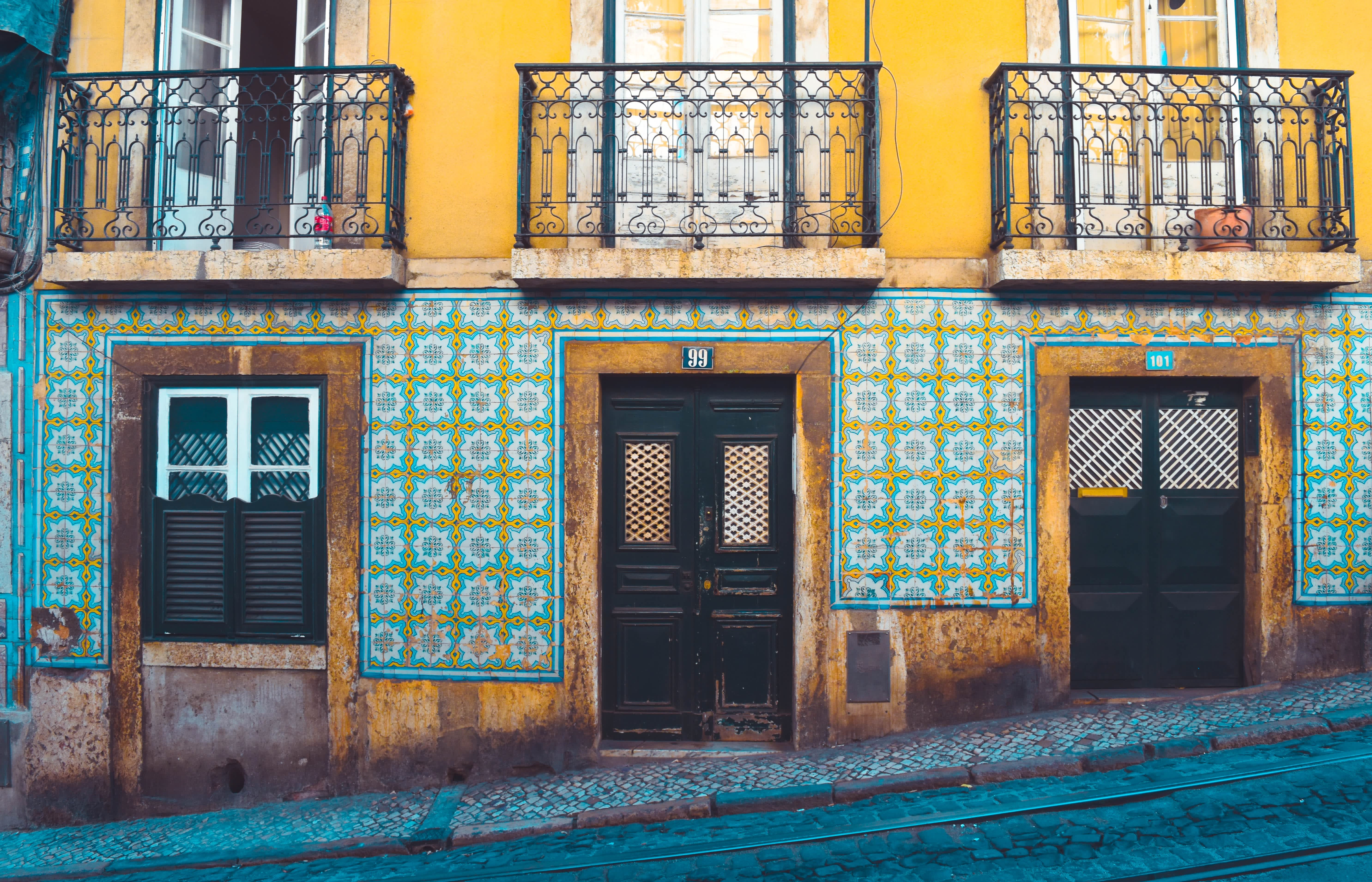 A traditional Lisbon building facade with colorful azulejo tiles, wrought iron balconies, and a cobblestone street.