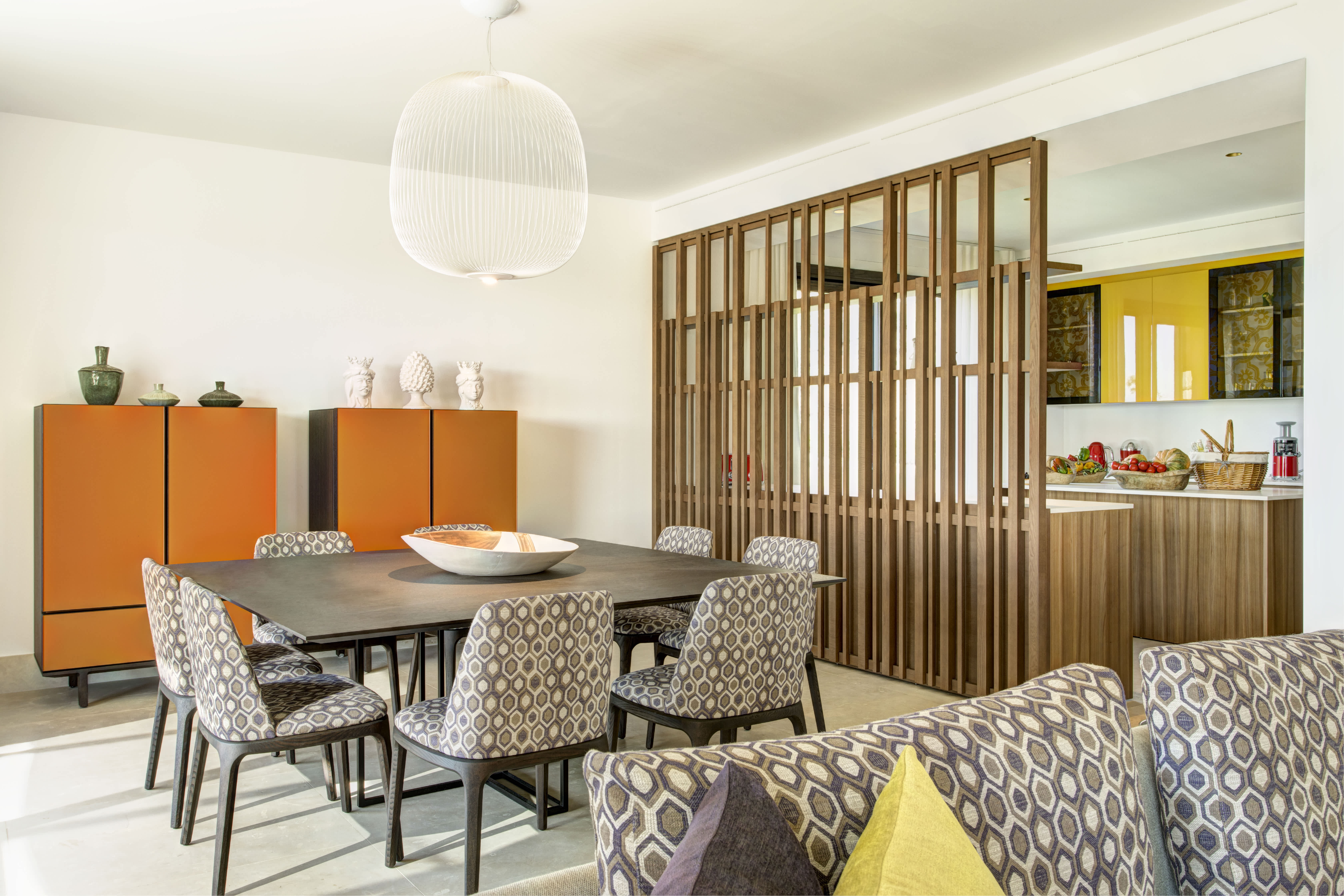 Elegant dining area in an Exclusive Resorts villa in Sicily, featuring modern decor with vibrant orange accents, geometric-patterned chairs, and a warm, open-concept design.