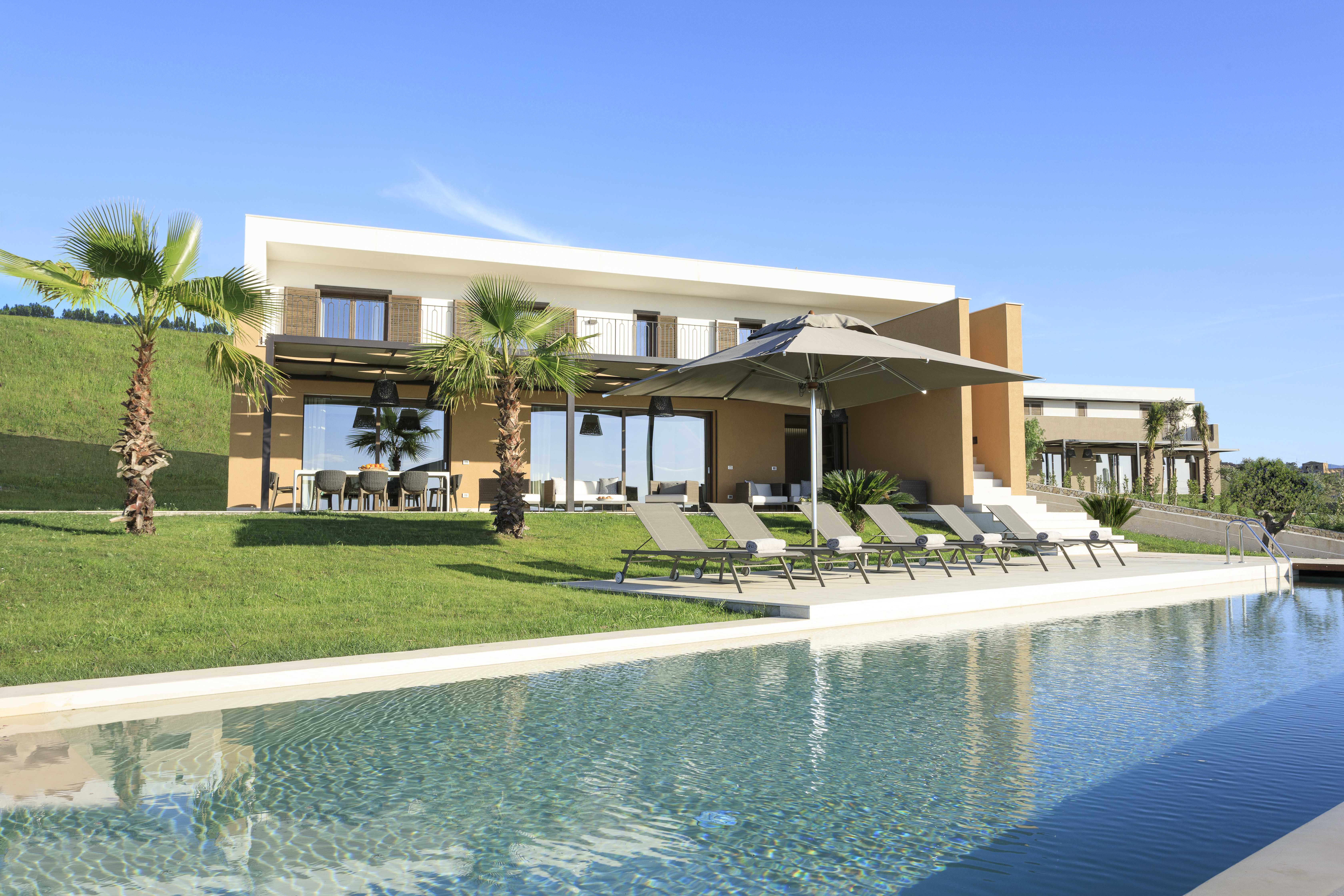 Luxurious Exclusive Resorts villa in Sicily featuring a private pool, sun loungers, and modern design surrounded by greenery under a clear blue sky.