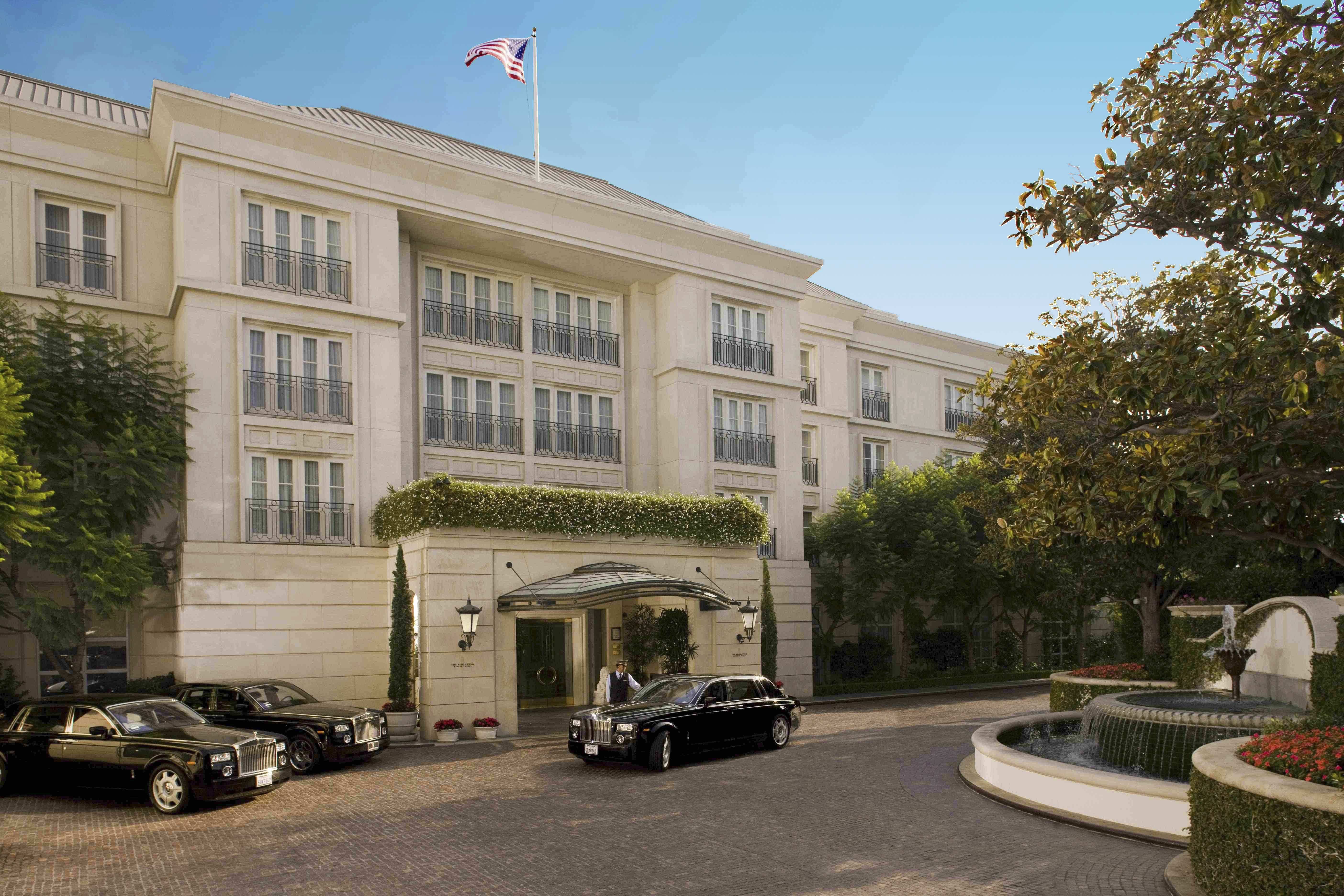 The grand entrance of The Peninsula Beverly Hills with luxury cars and a fountain.