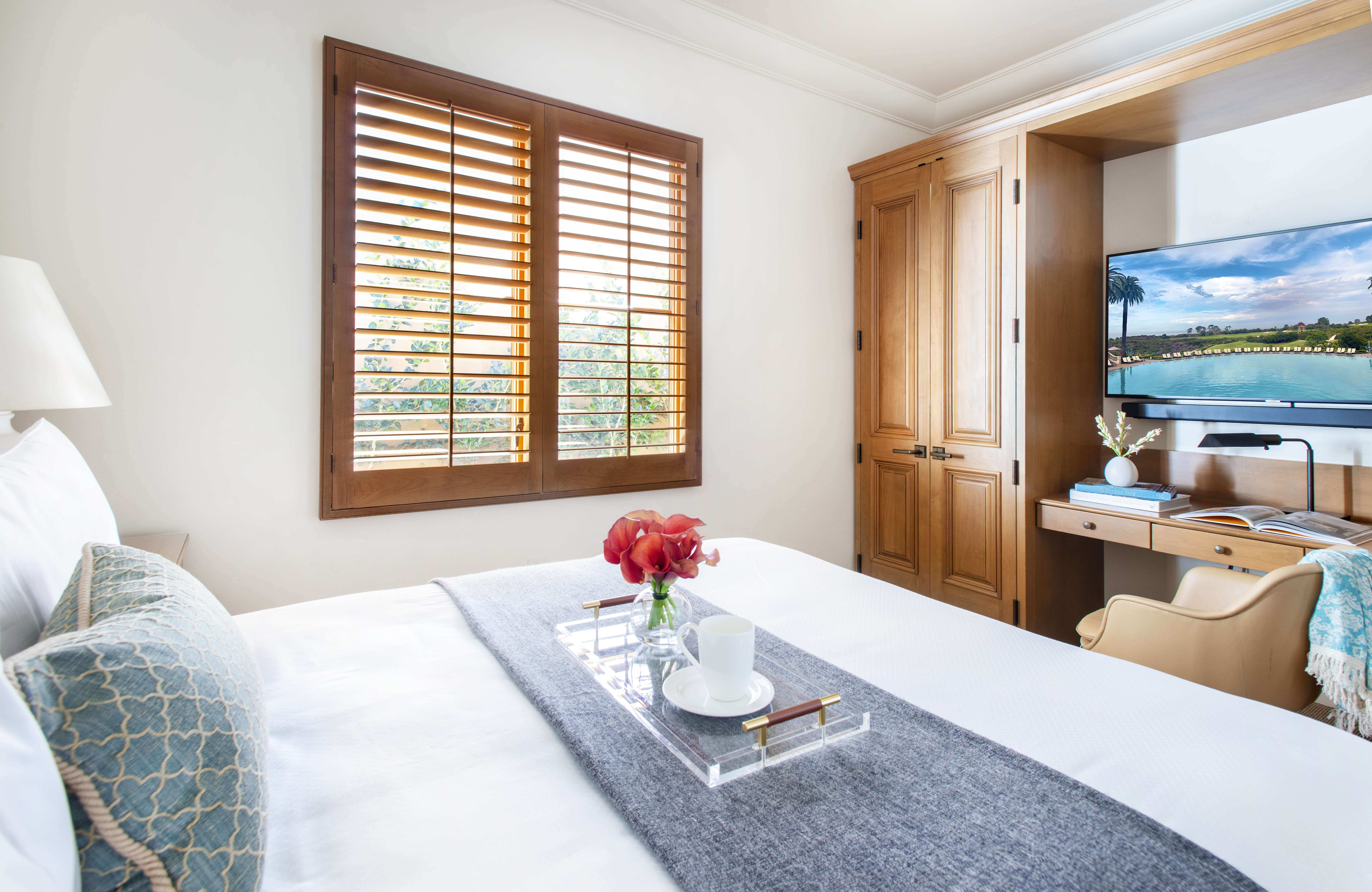 Bedroom with a plush bed, wooden shutters, and a work desk at a Pelican Hill Resort property by Exclusive Resorts.