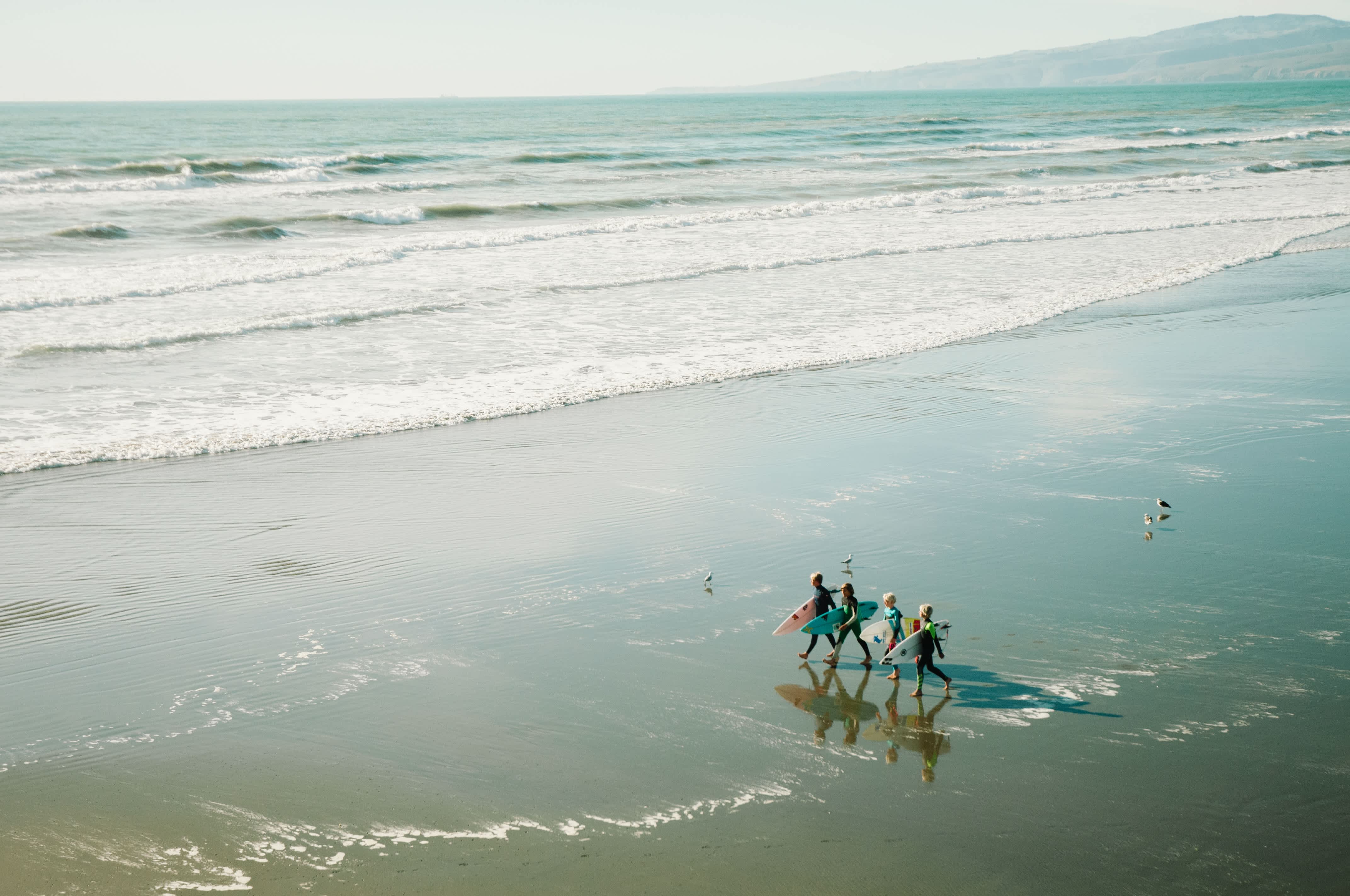 Children walking and holding surfboards on the beach.