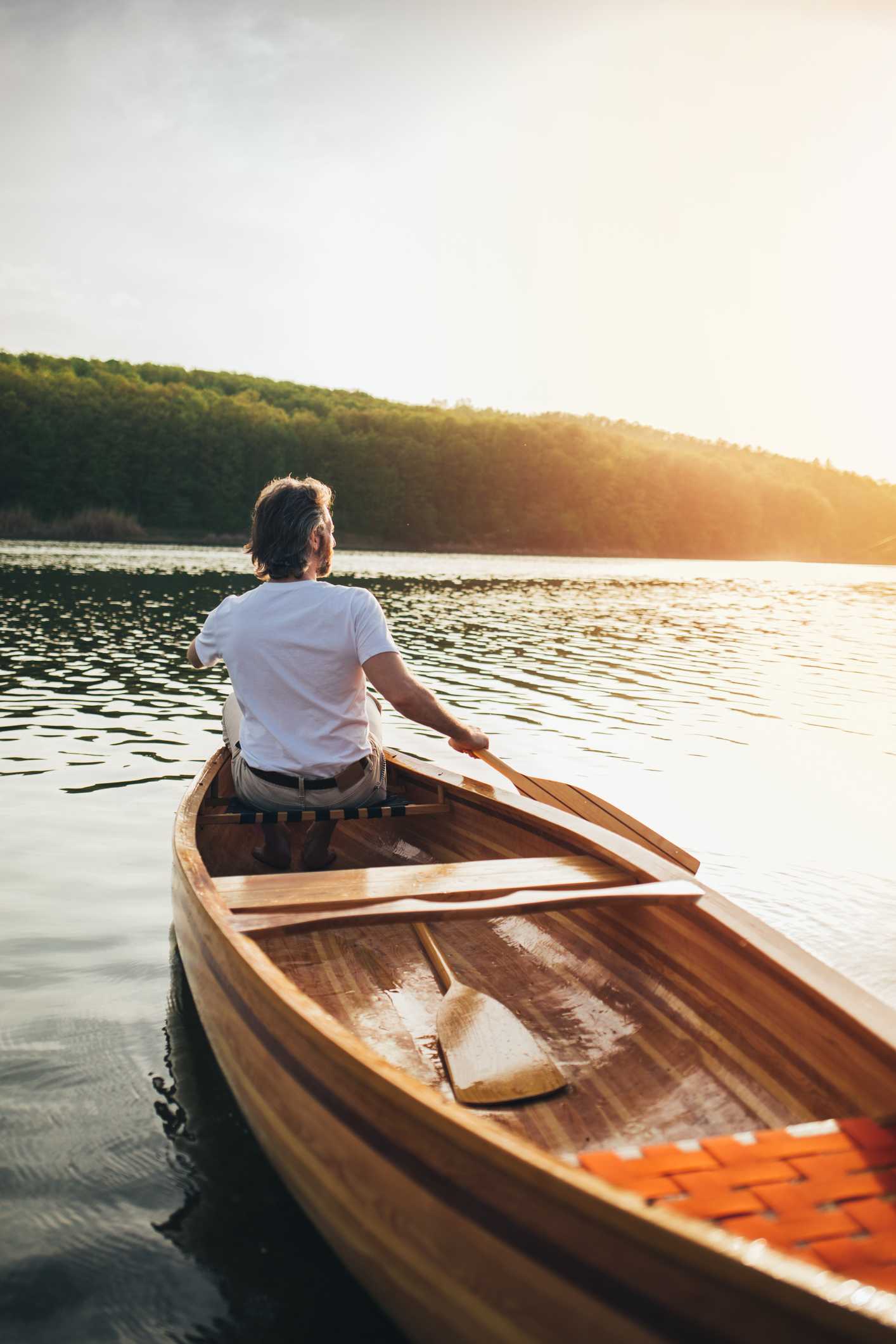 Man rowing a wooden boat on a serene lake in Provence during sunset.