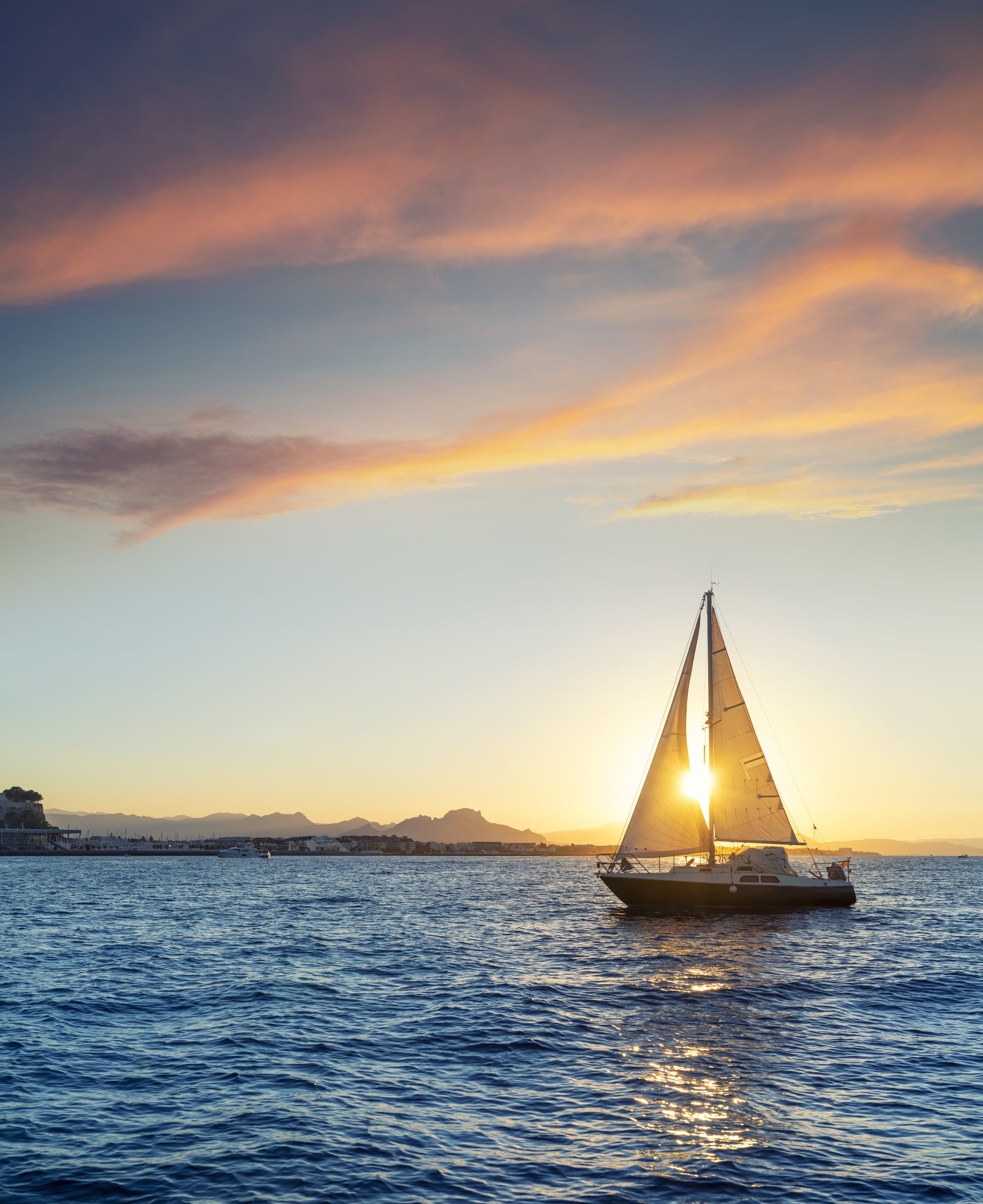 Sailboat on the water at sunset with colorful clouds in the sky.