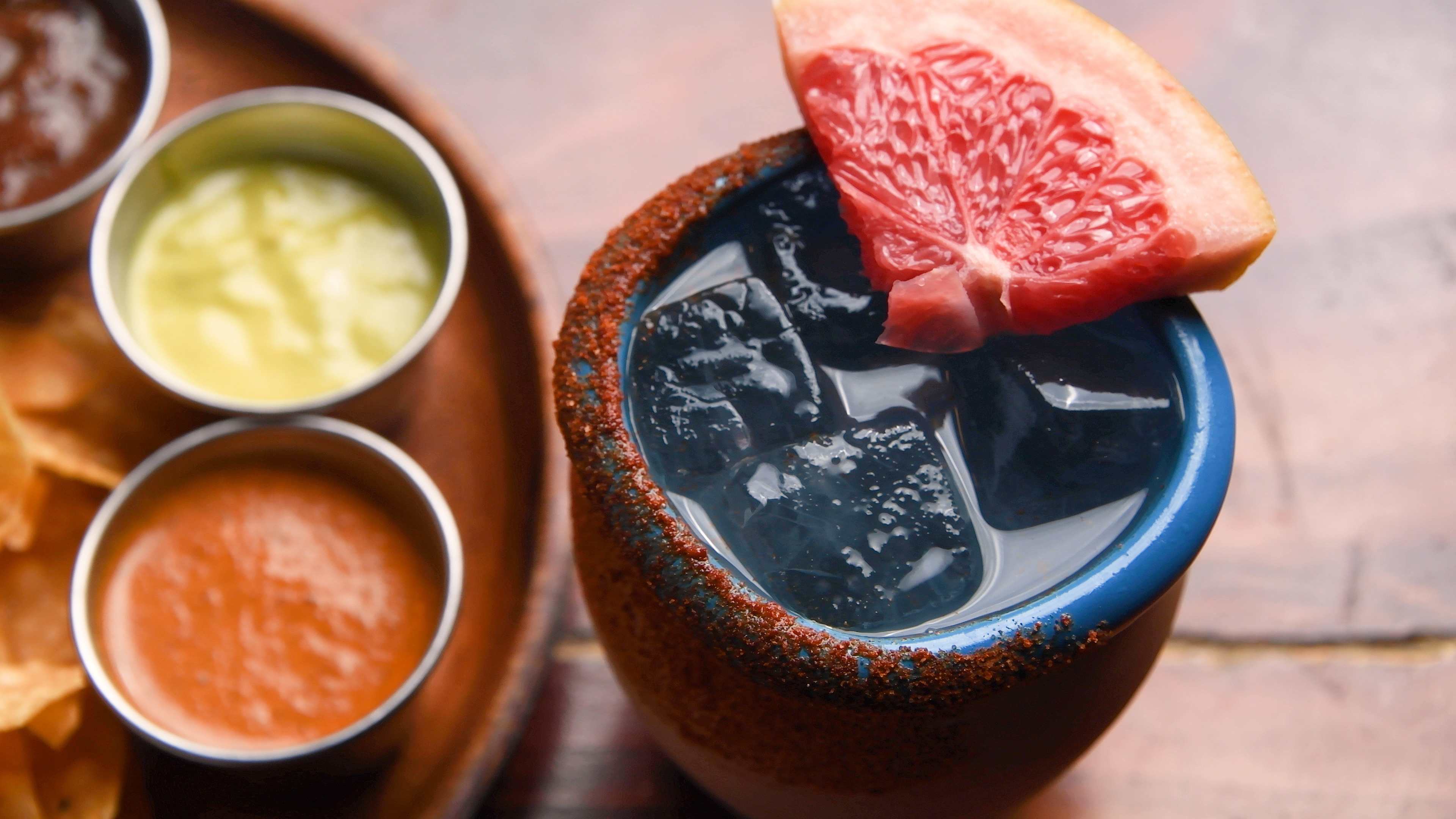 Close-up of a refreshing drink garnished with a grapefruit slice, served with salsas and chips on the side.