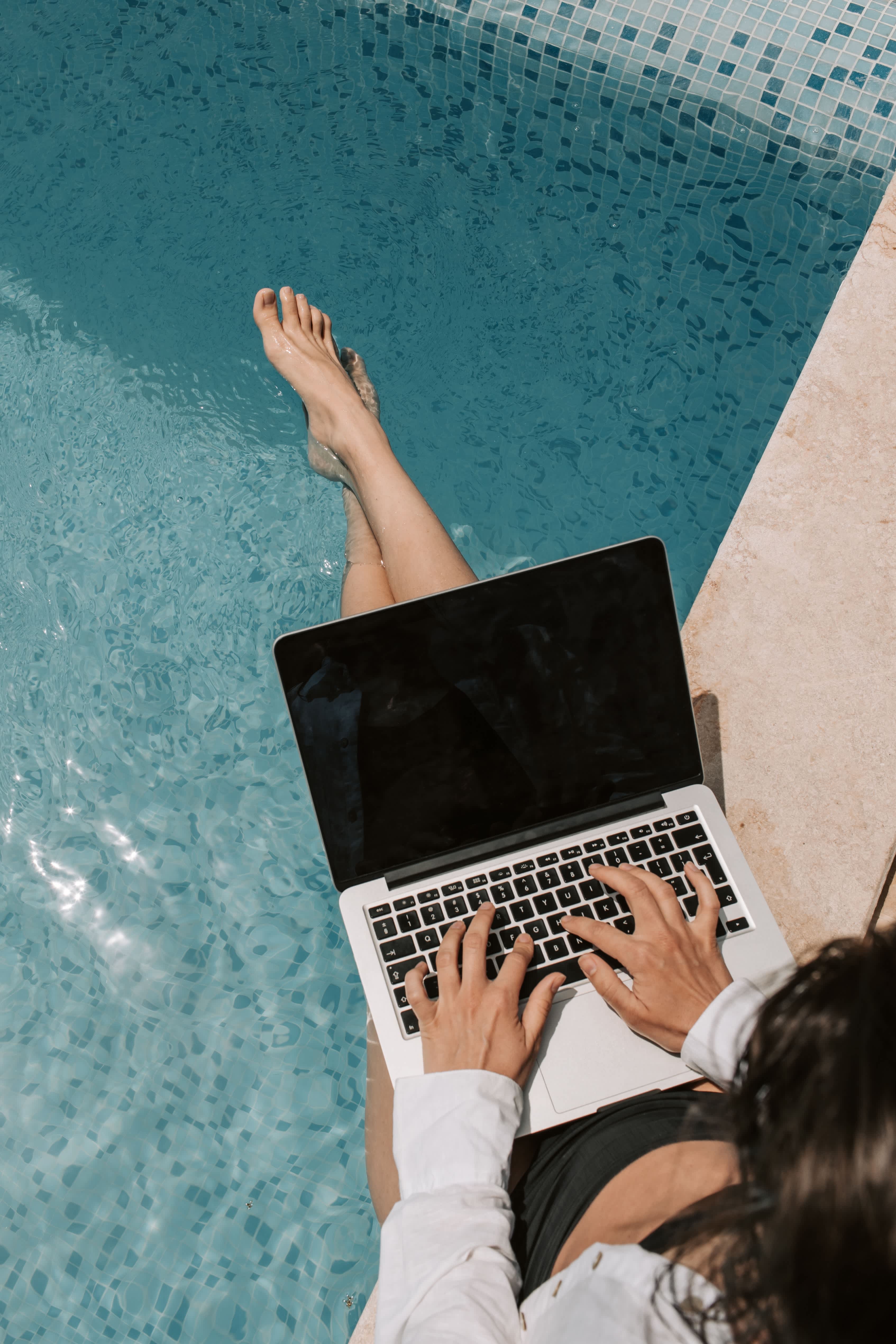 Woman on laptop by pool.