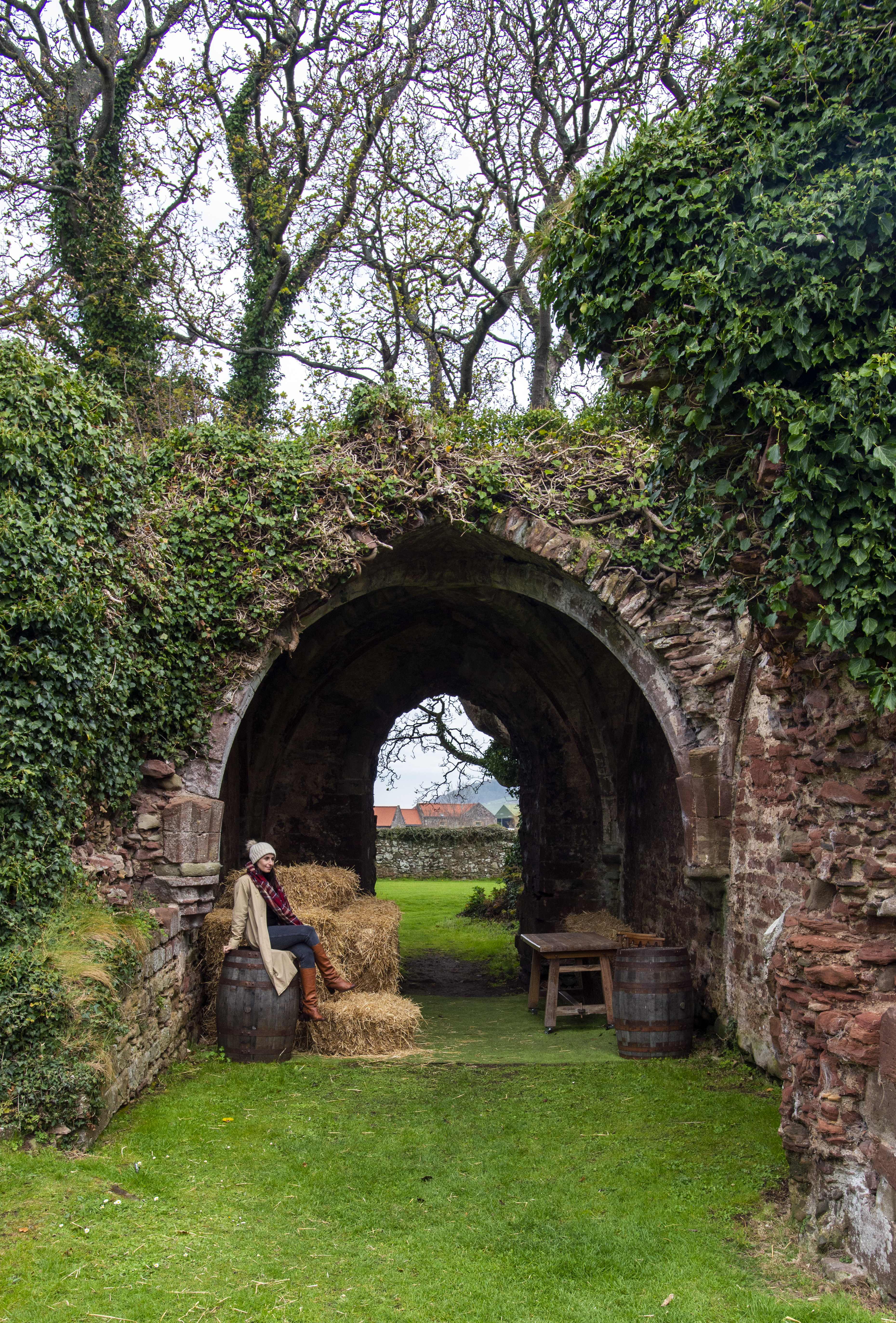 A woman sitting under a green overgrown walkway.