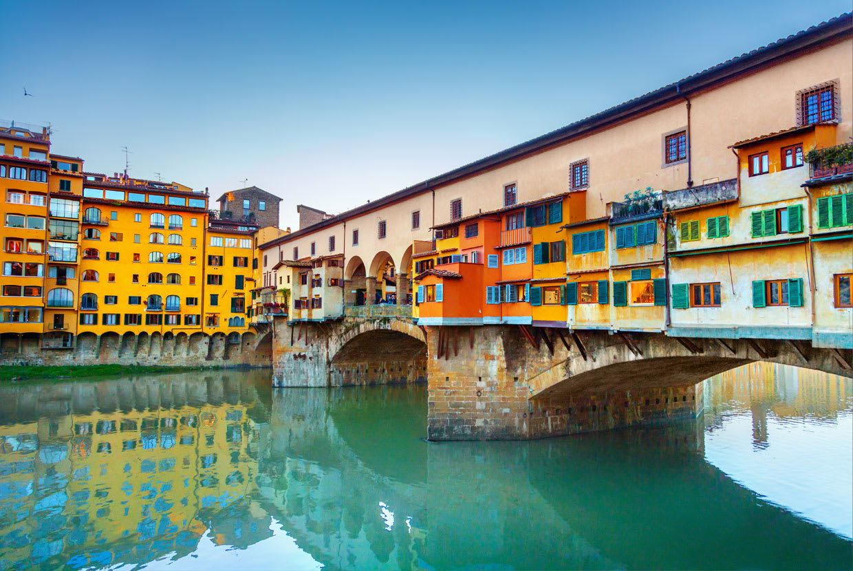 Colorful buildings on the Ponte Vecchio bridge reflecting in the Arno River in Florence, Italy.
