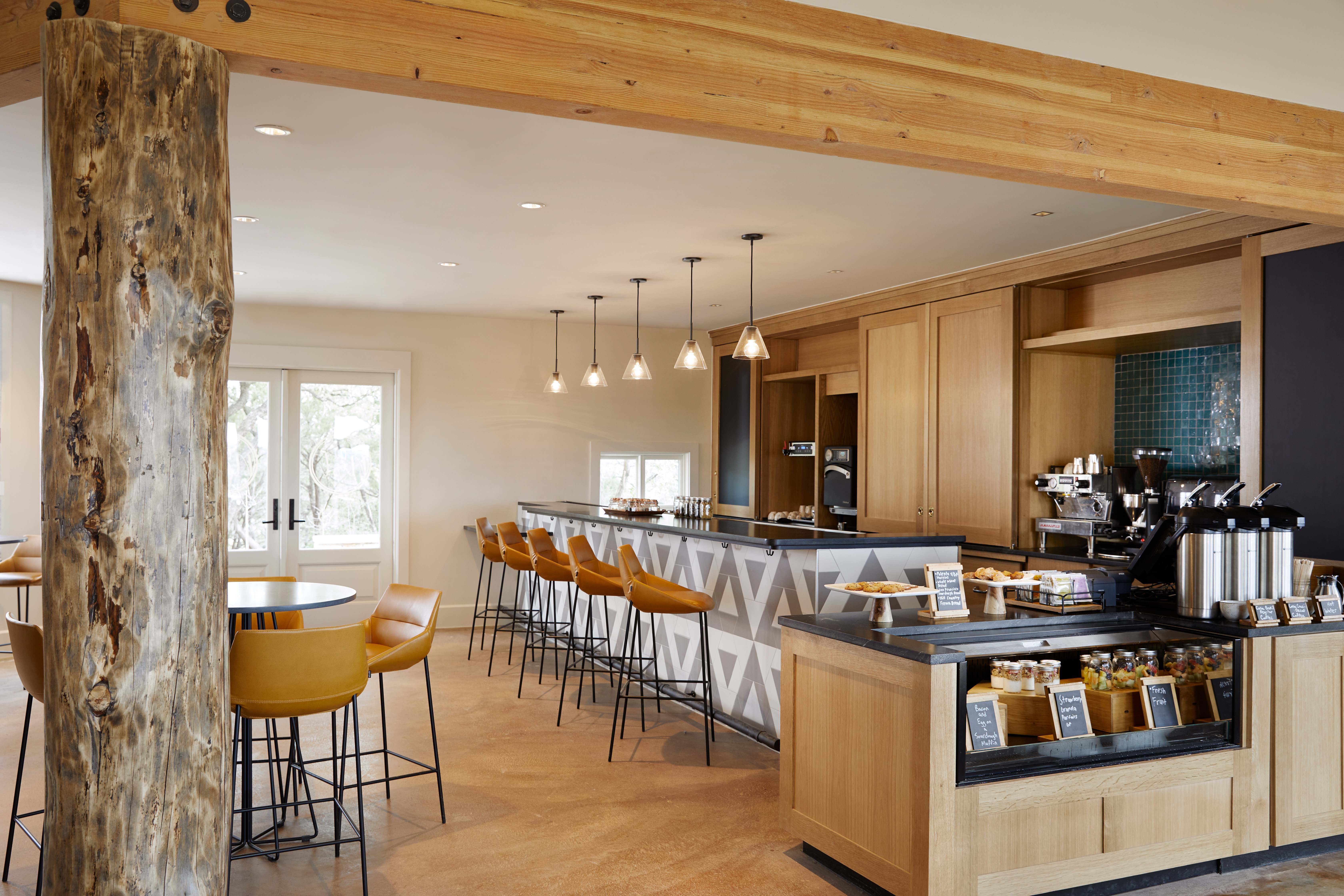 Modern café at Miraval Resort with natural lighting, wooden accents, bar seating, pendant lights, and a coffee station.