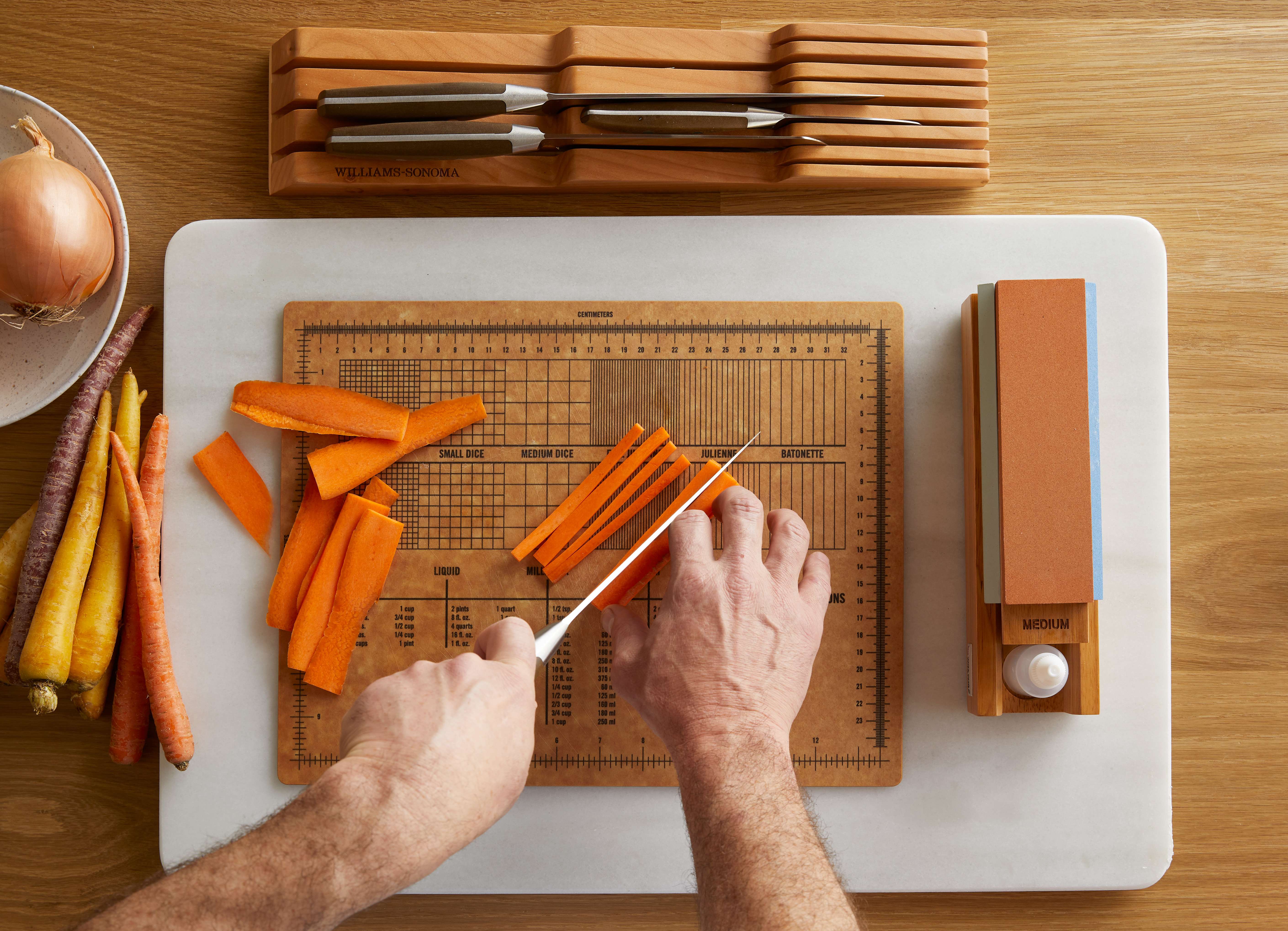 Overhead view of a person cutting carrots on a wooden chopping board with measurement guides.