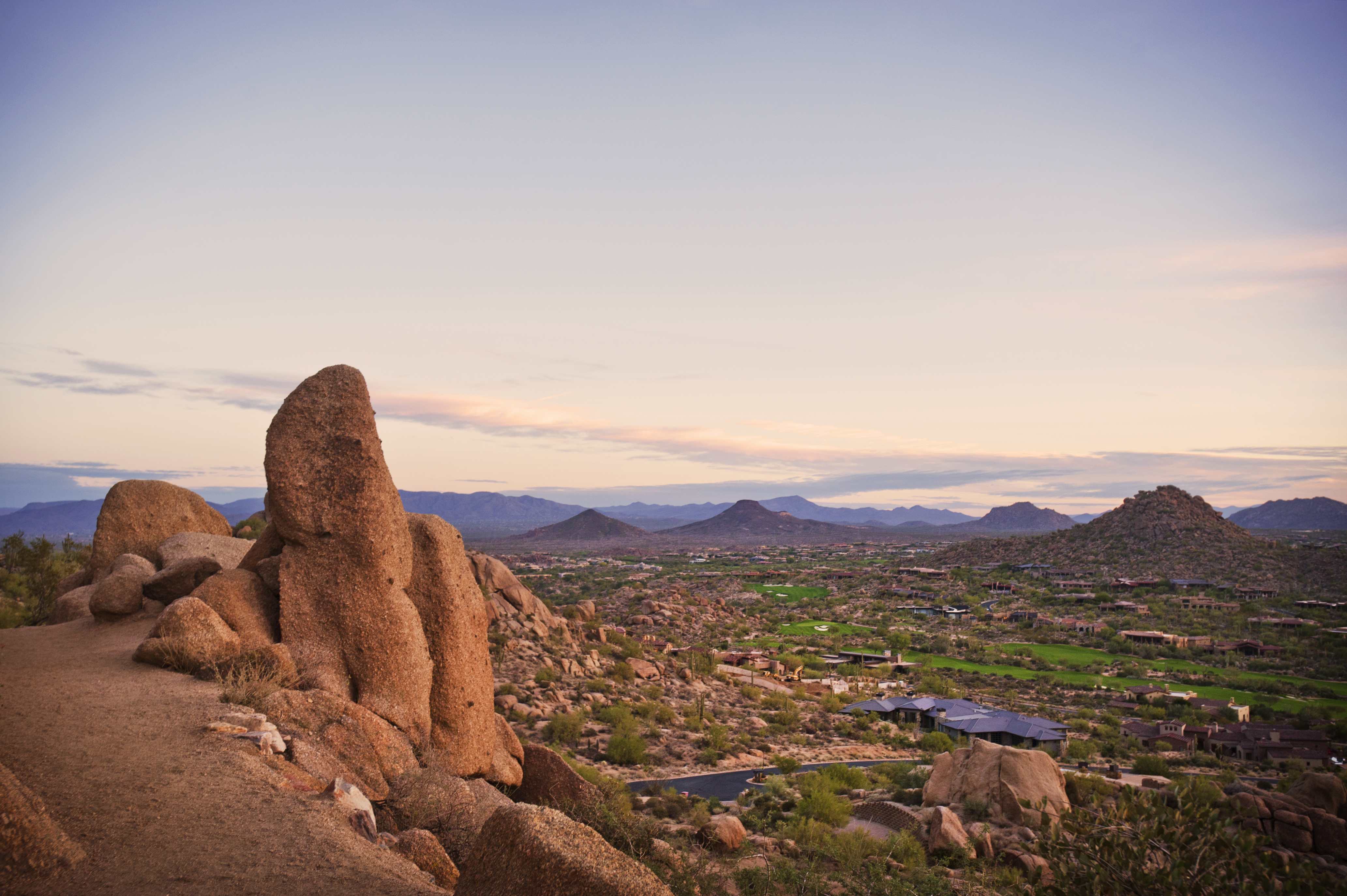 View of Scottsdale, Arizona, from a rocky hilltop during sunset with mountains in the background.