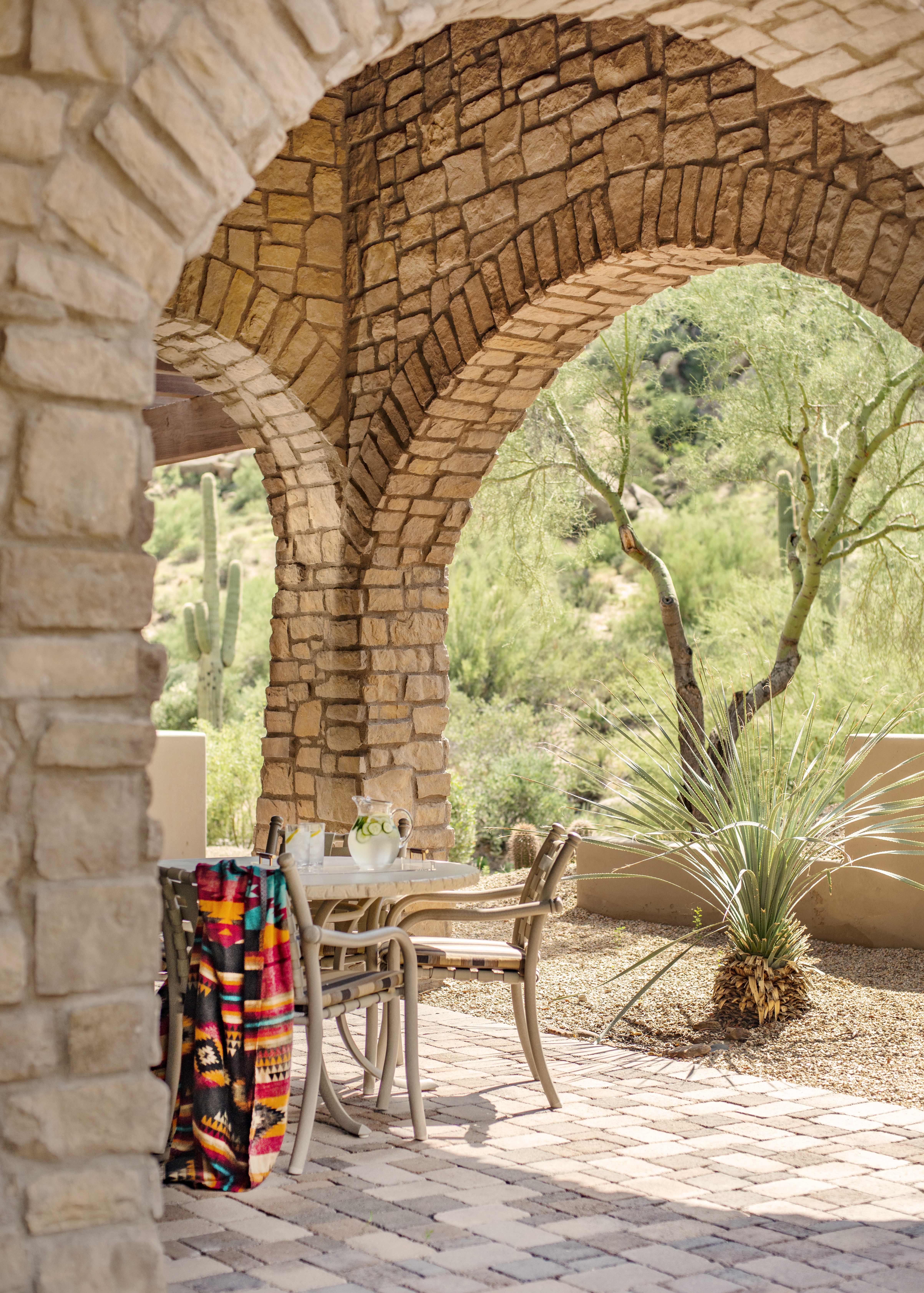 Stone archway leading to an outdoor seating area at an Exclusive Resorts' private home in Scottsdale at The Rocks Club, with desert vegetation in the background.