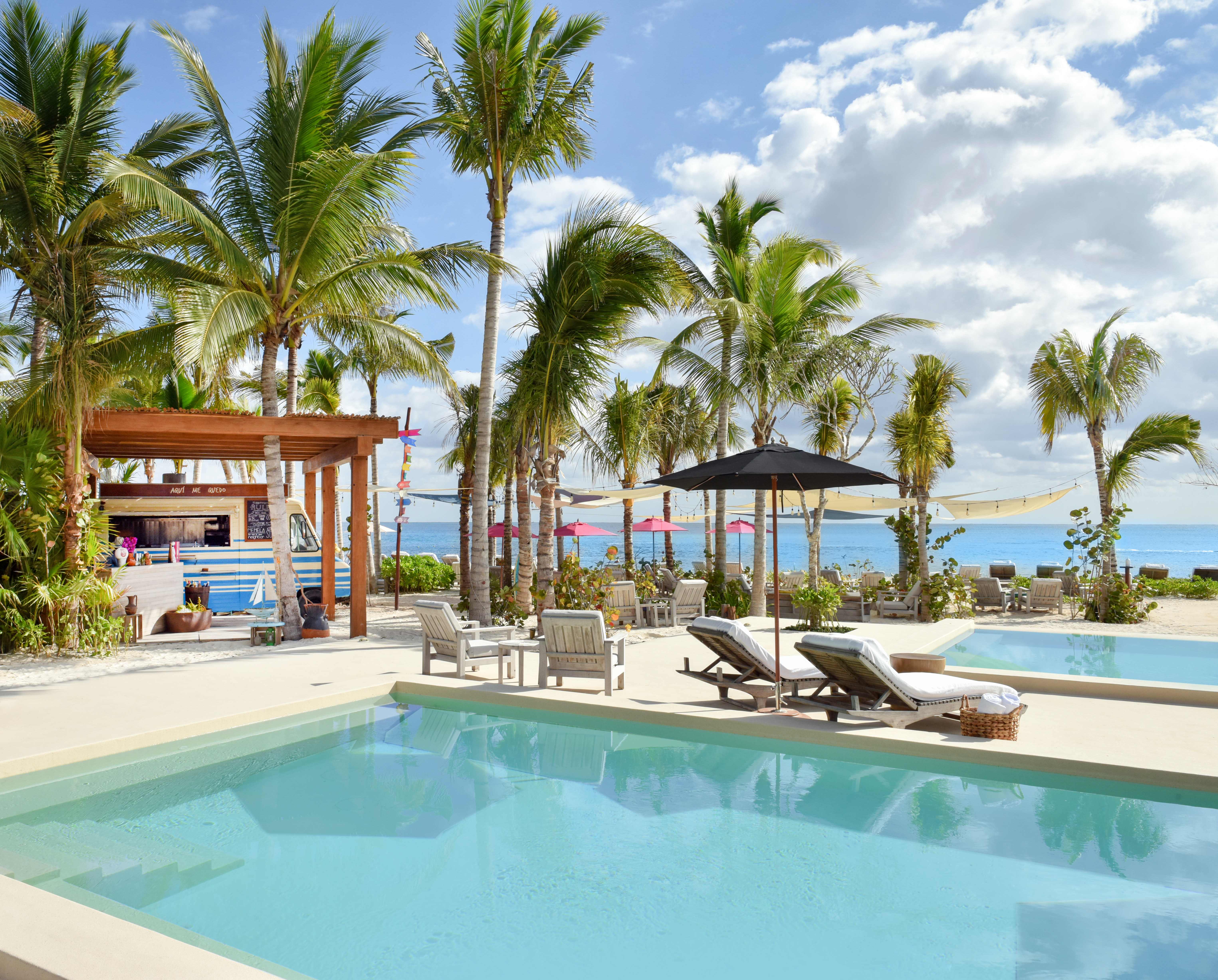Resort pool near Exclusive Resorts properties at Rosewood Mayakoba, featuring a beach bar, palm trees, and ocean views.