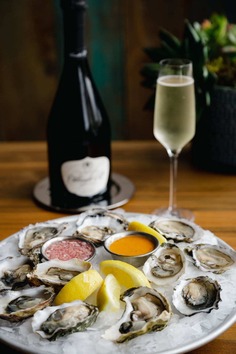 A plate of oysters with lemon wedges and sauces, accompanied by champagne.