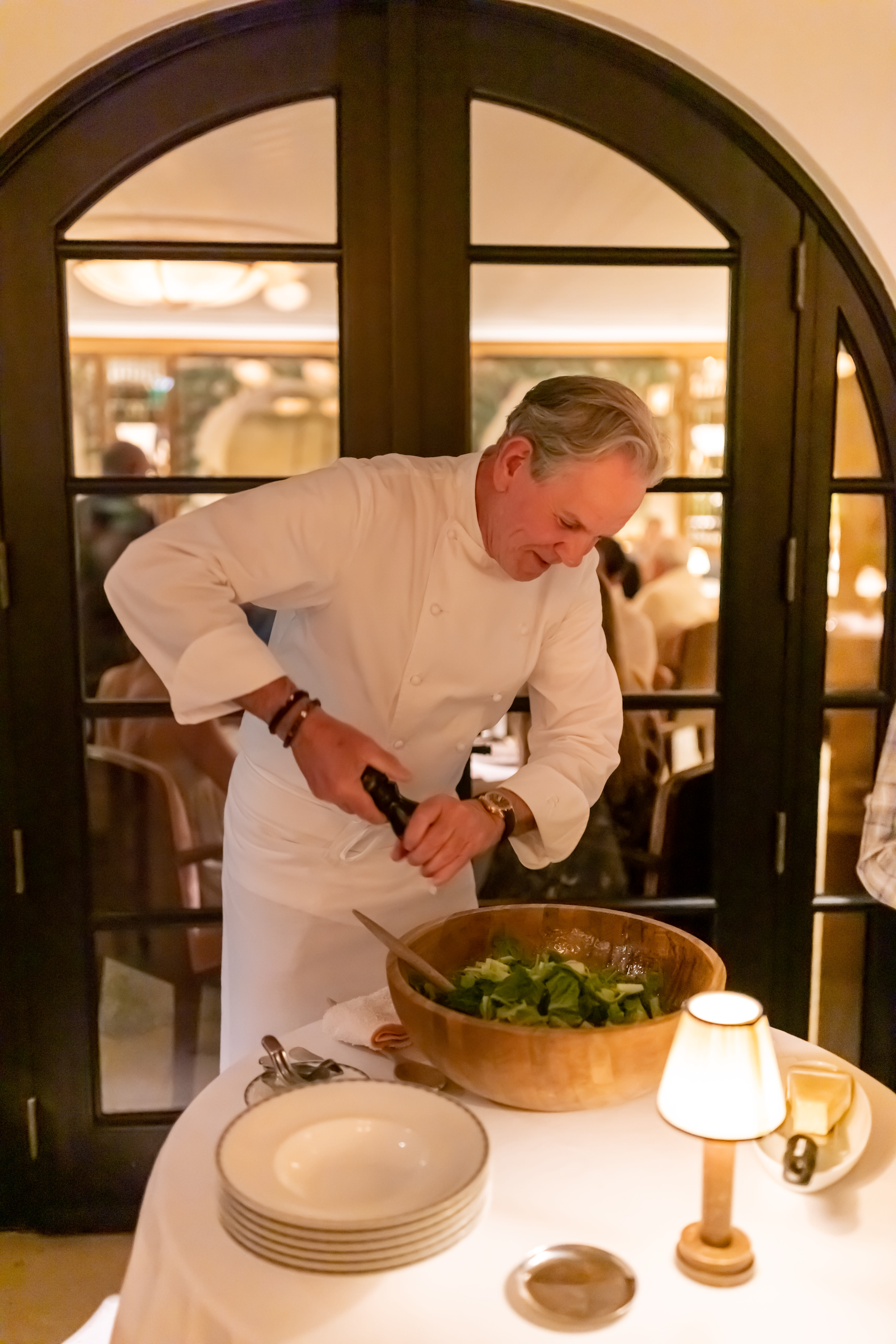 A chef preparing a fresh salad at the table, seasoning it with a pepper grinder.