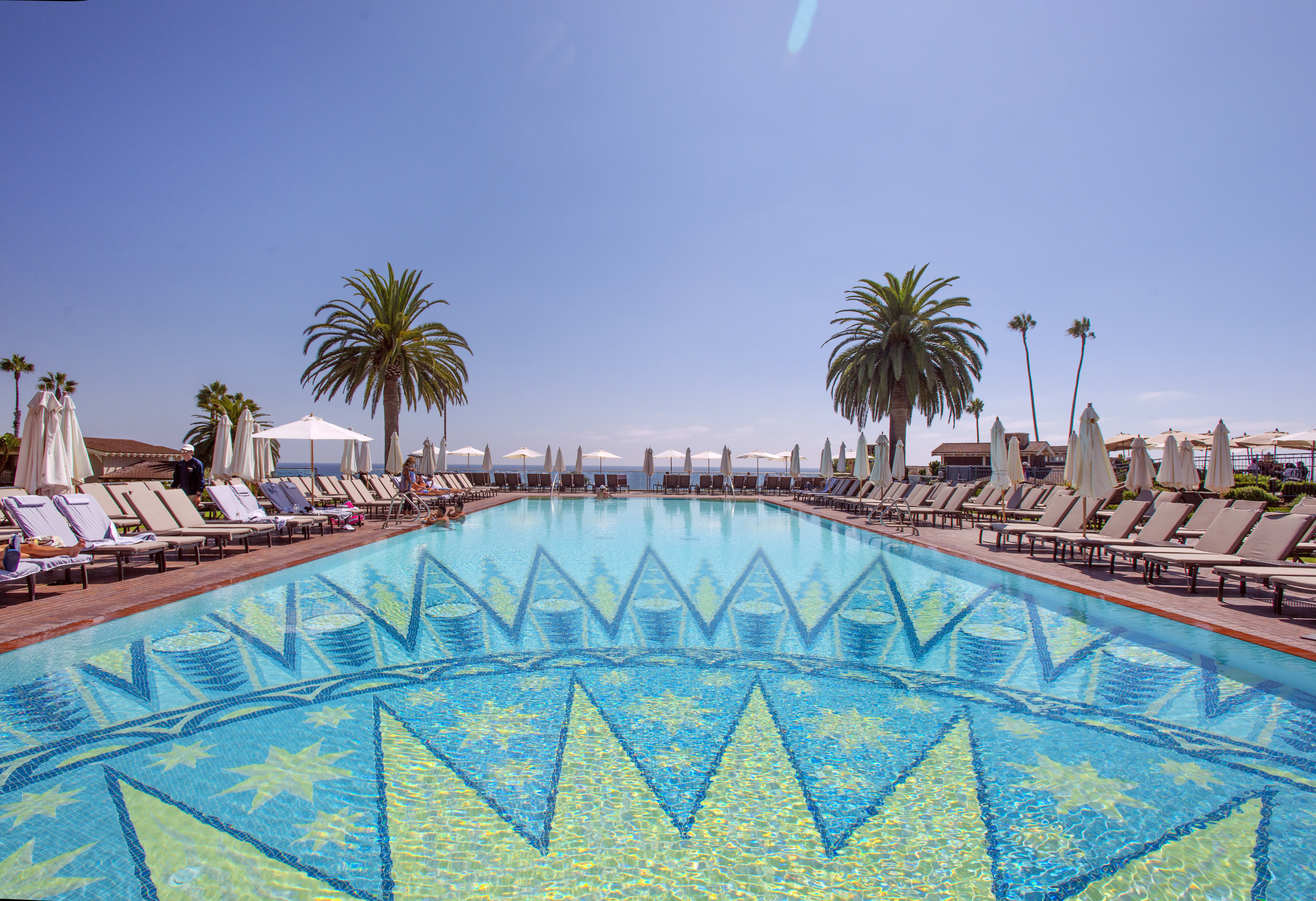 Luxurious poolside at Montage Laguna Beach with palm trees and ocean view in the background.