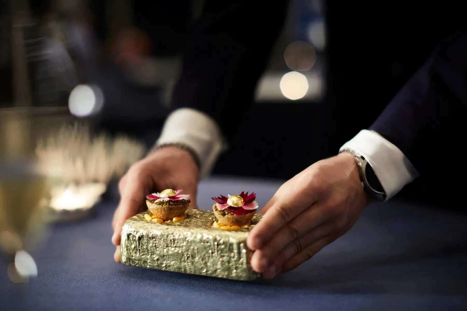 Close-up of a waiter serving an elegant dish with edible flowers in a fine dining restaurant.
