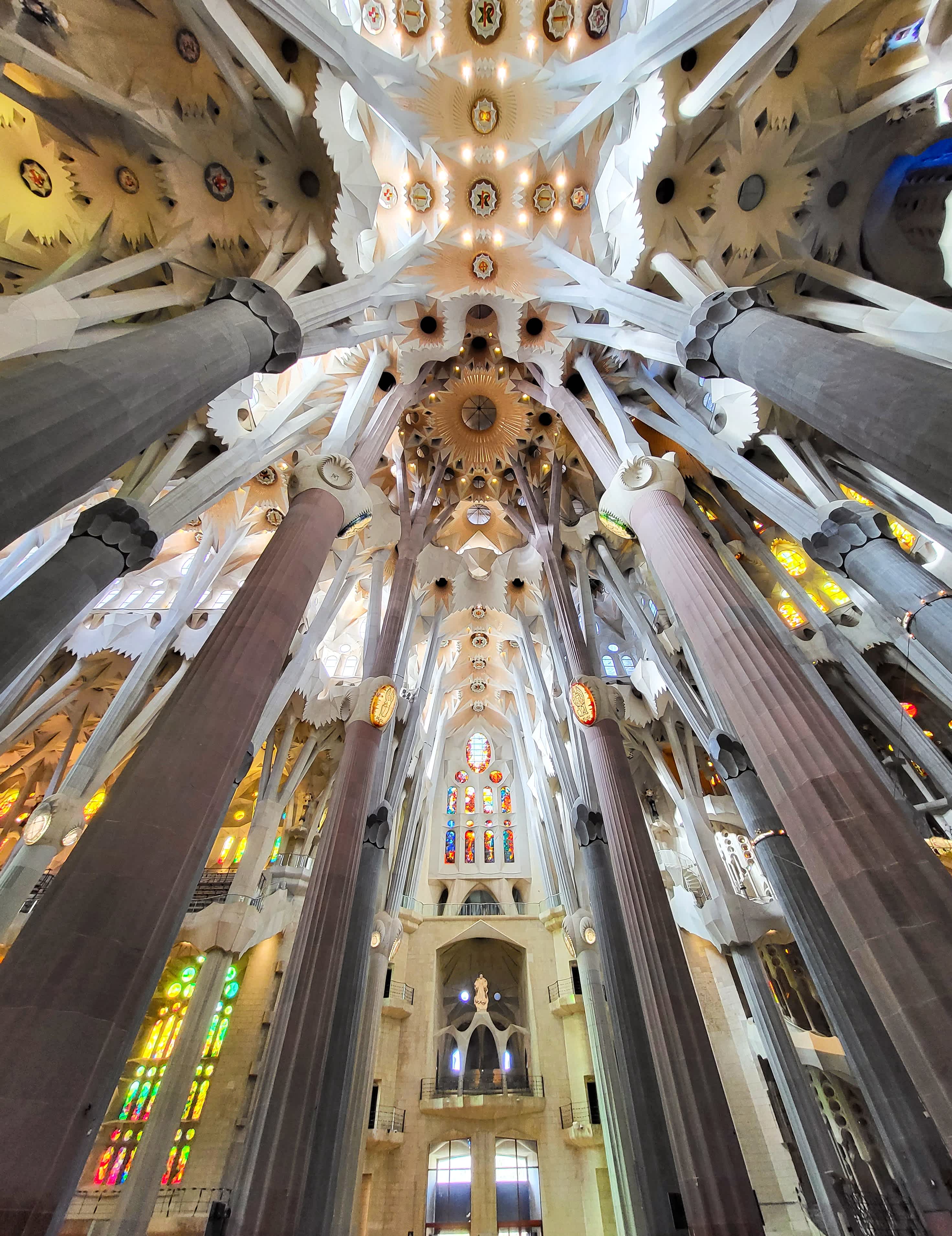 Interior view of the Sagrada Família's nave in Barcelona, showcasing the towering columns, vaulted ceilings, and colorful stained glass windows.