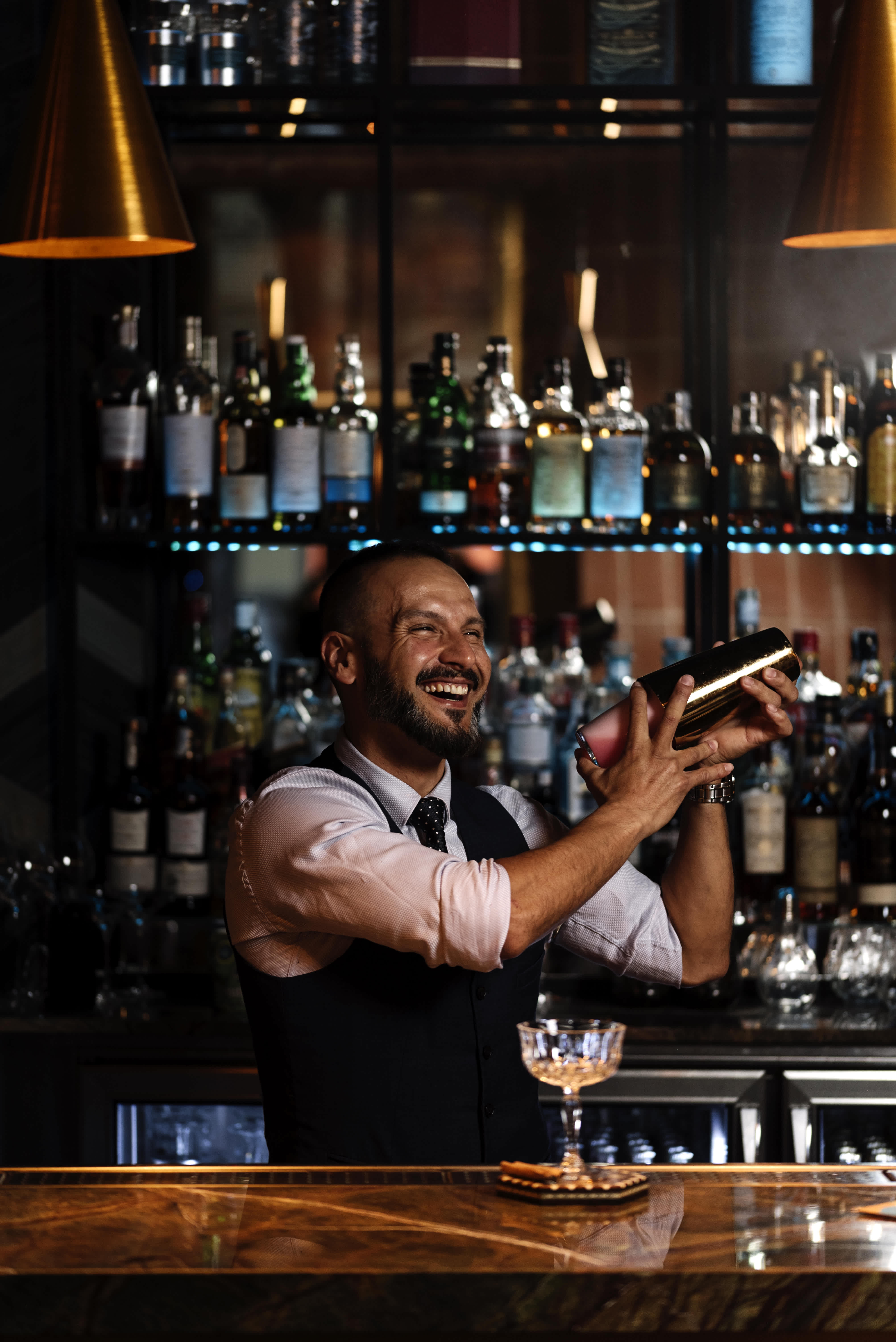 Cheerful bartender shaking a cocktail mixer at a bar with a warm ambient light.