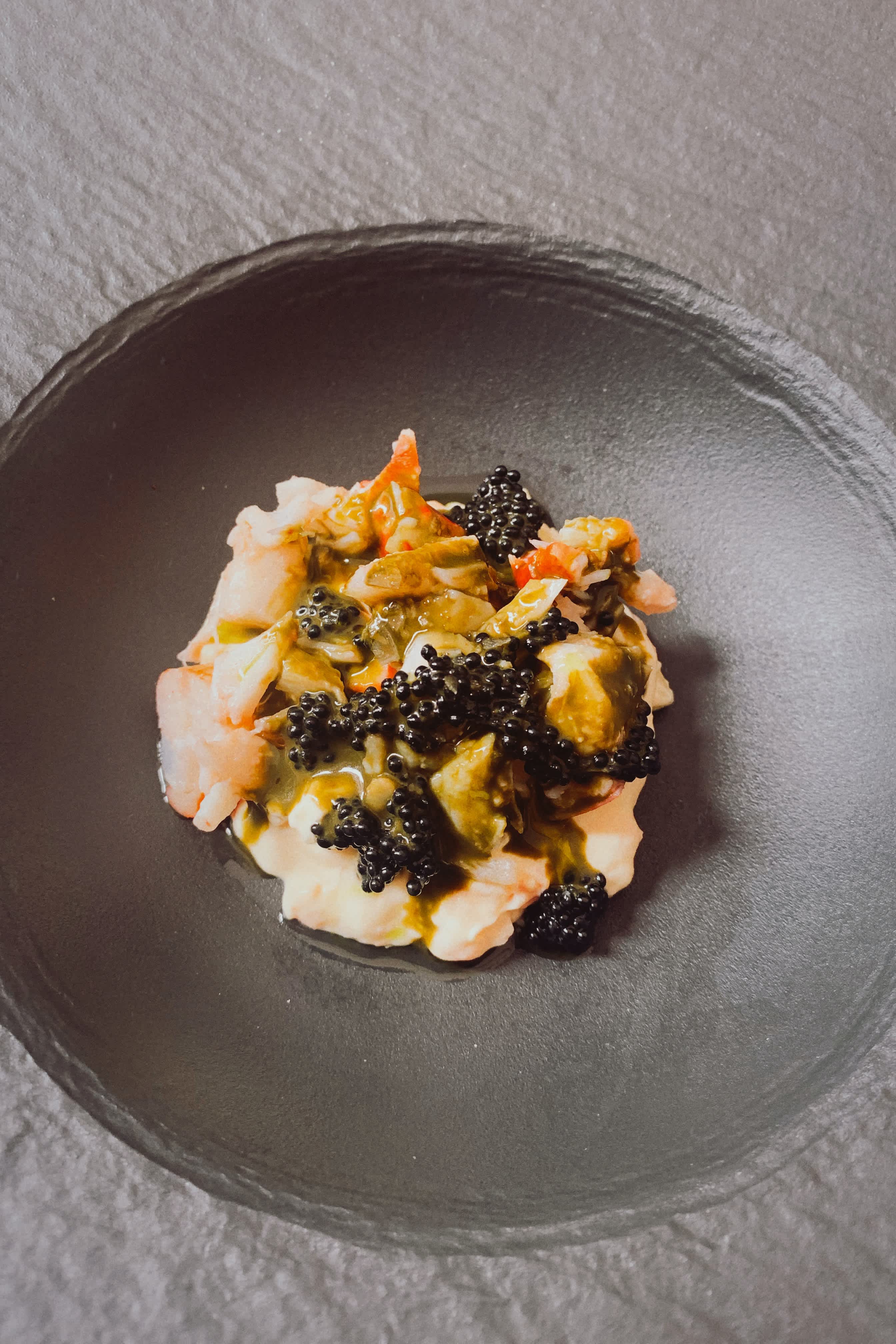 Gourmet dish with shrimp, caviar, and a creamy sauce served on a dark plate