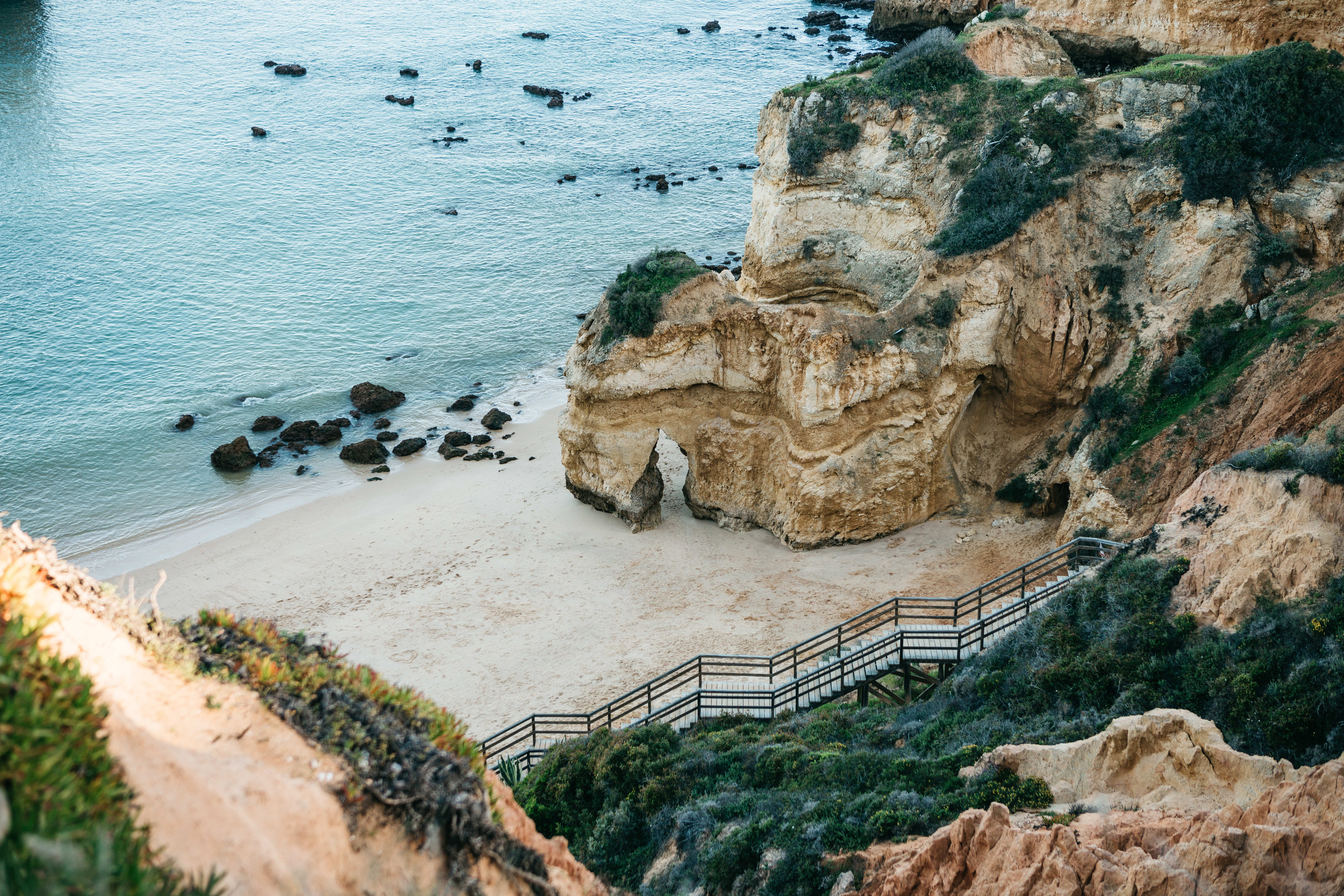 Aerial view of a secluded beach with rock formations and a wooden walkway in Algarve, Portugal.