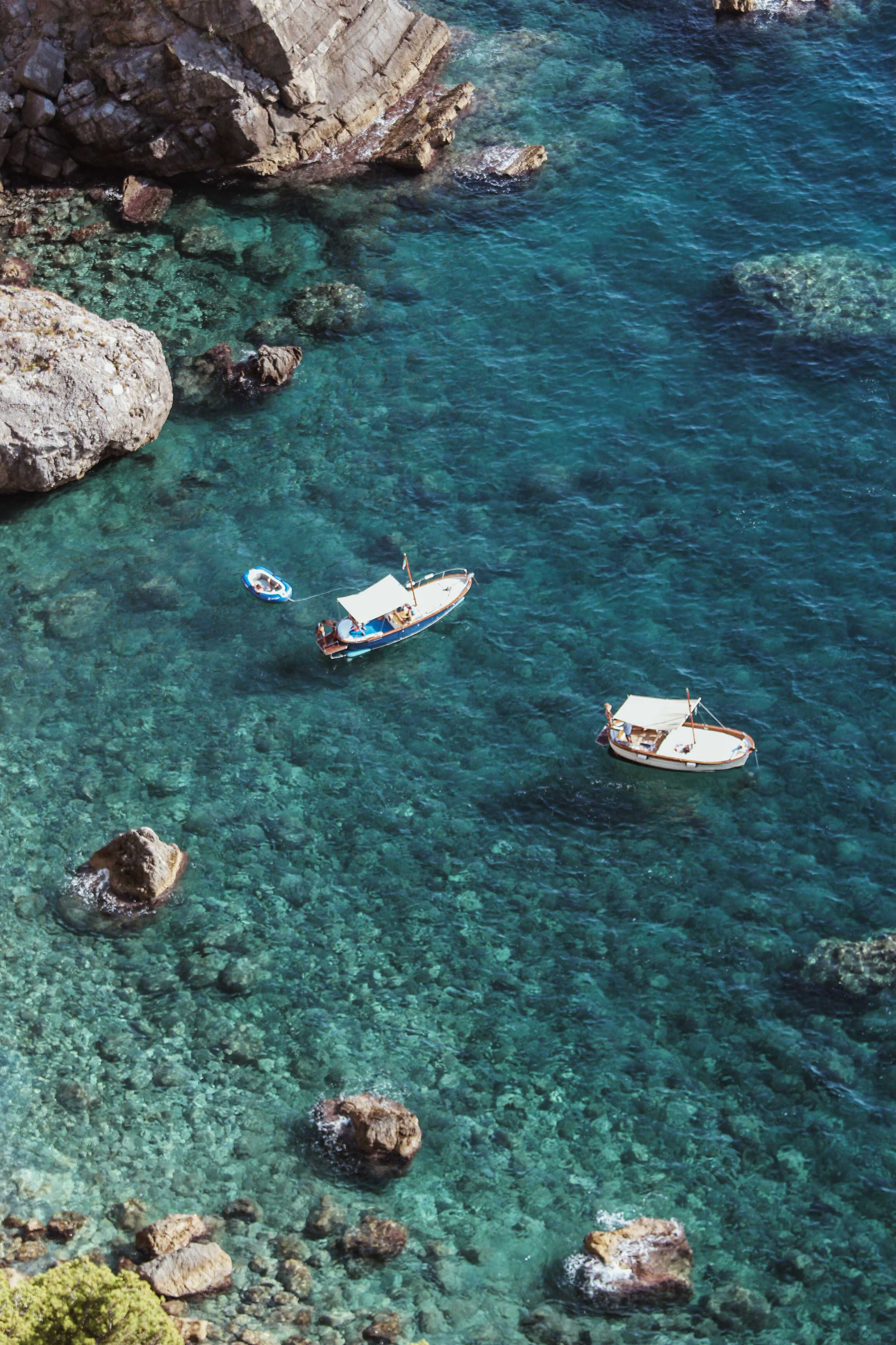 Boats floating on the clear turquoise waters near the rocky shores of the Amalfi Coast.