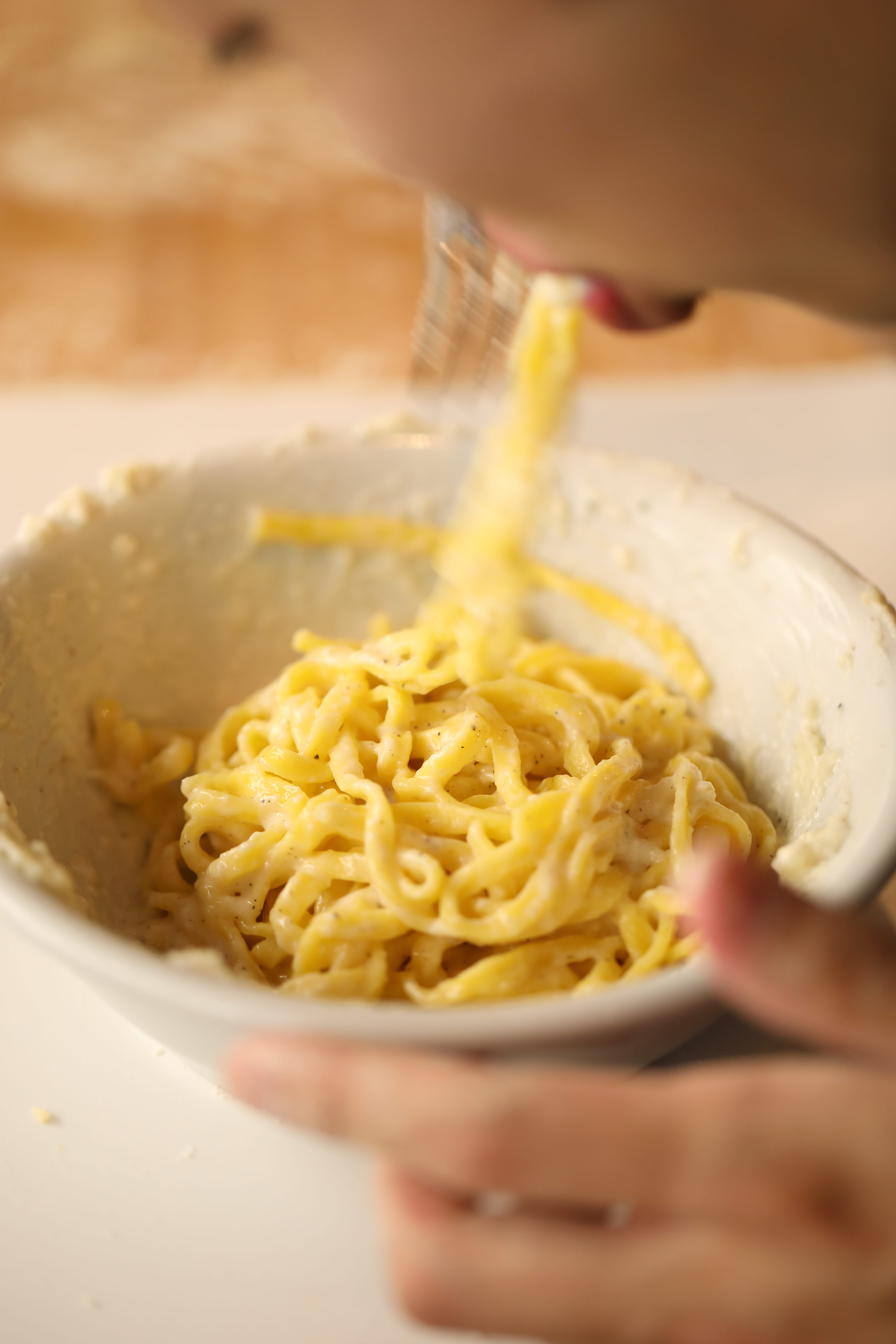Freshly prepared pasta being mixed in a creamy sauce.