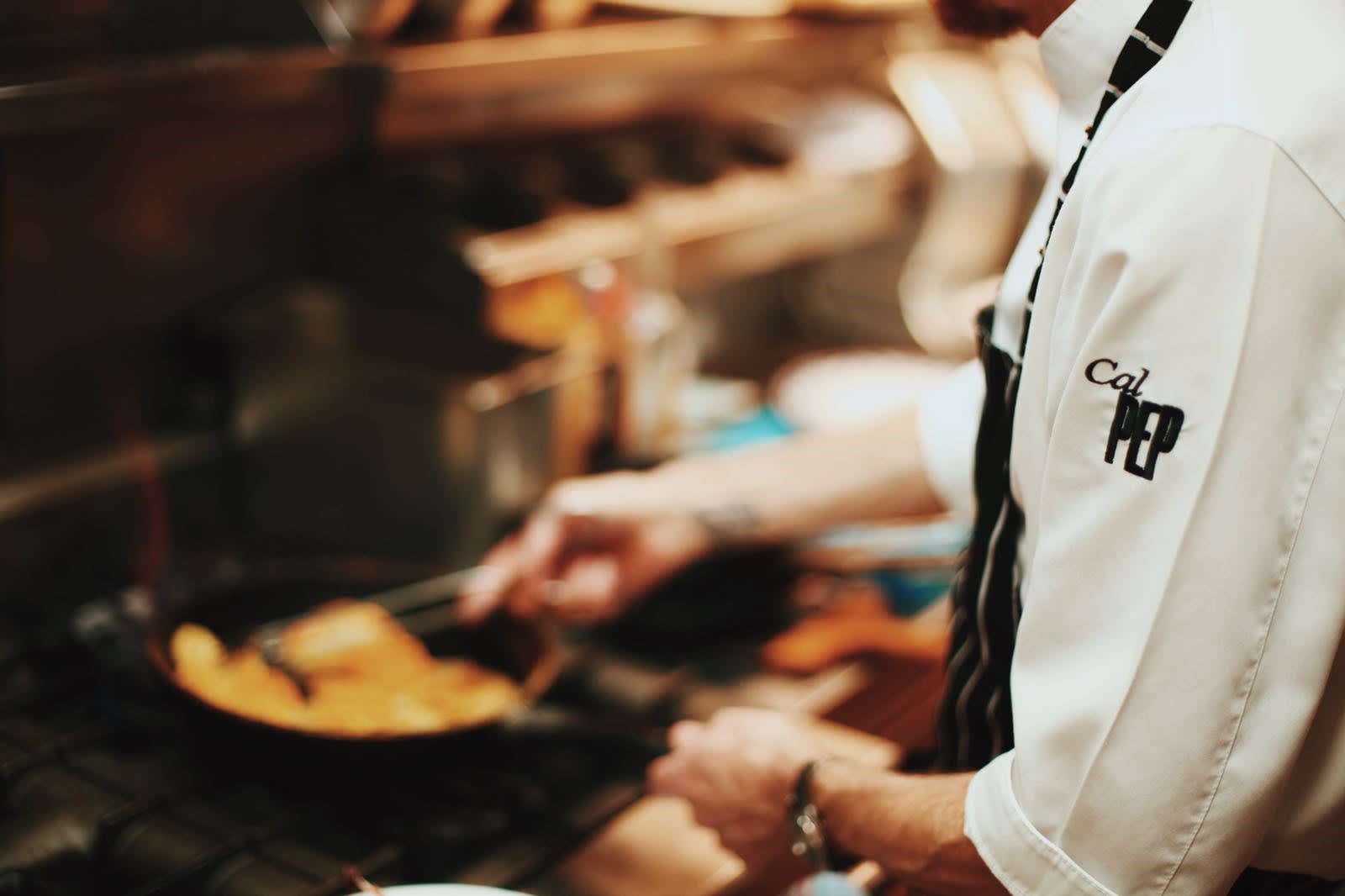 A chef at Cal Pep expertly sautés food in a pan over a commercial kitchen stove, in Barcelona.