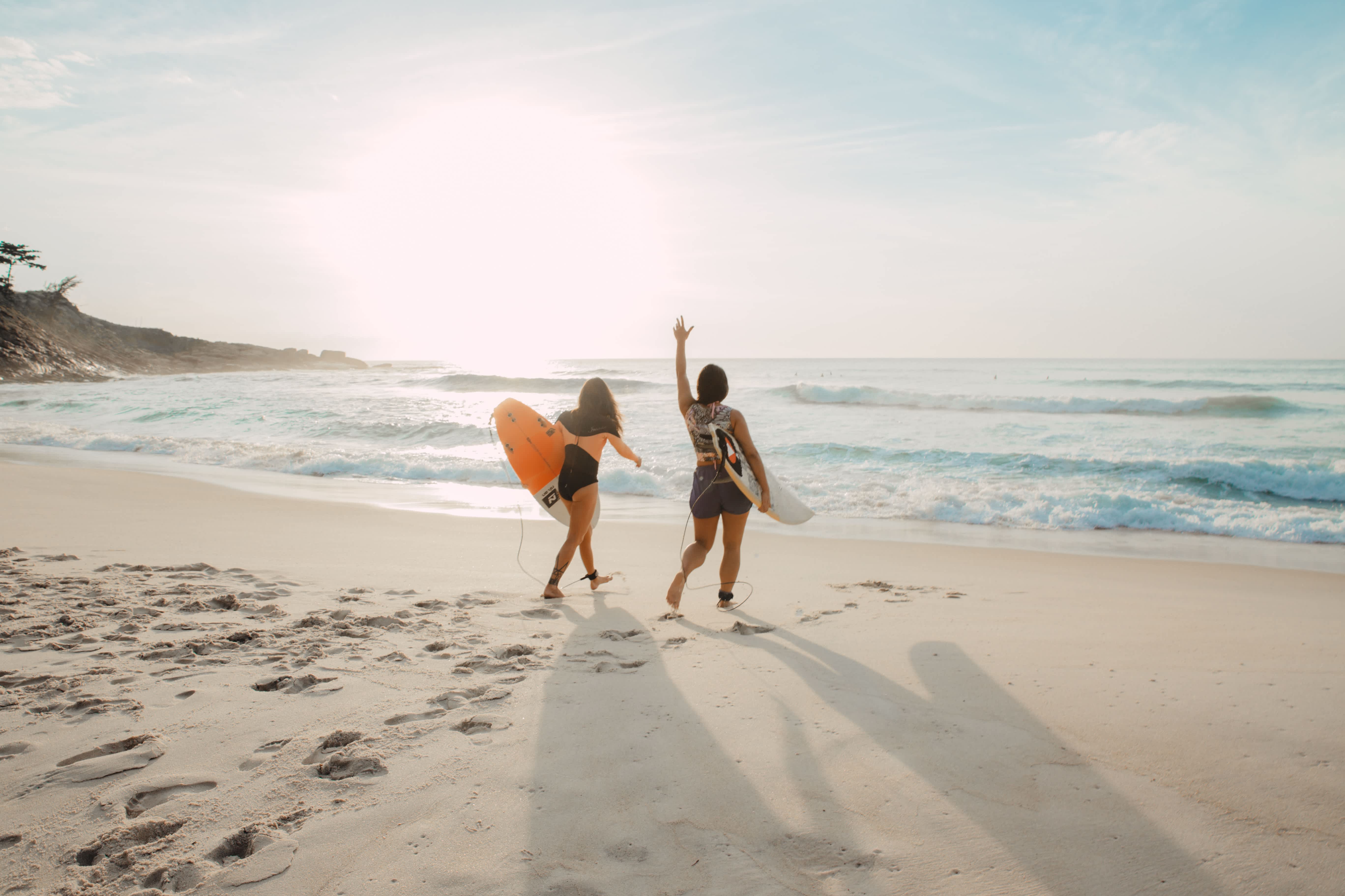 Two surfers walking on a San Sebastian beach at sunset with surfboards in hand.