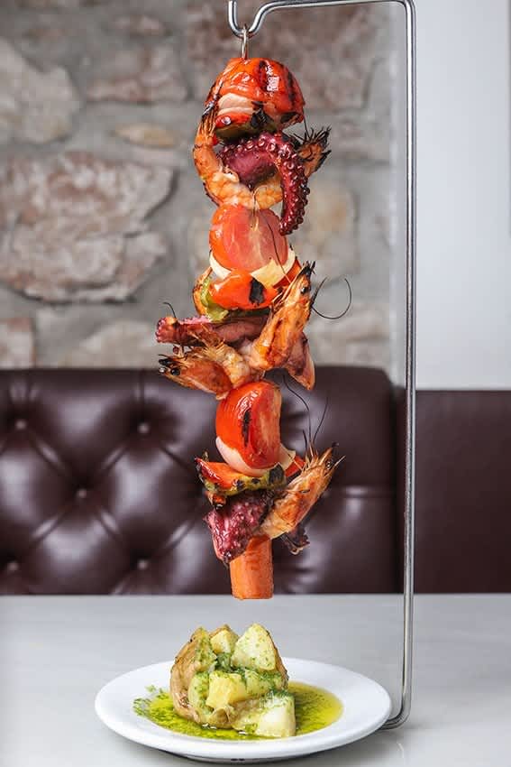 Grilled seafood skewer with shrimp, octopus, and vegetables served with baked potato and herb sauce