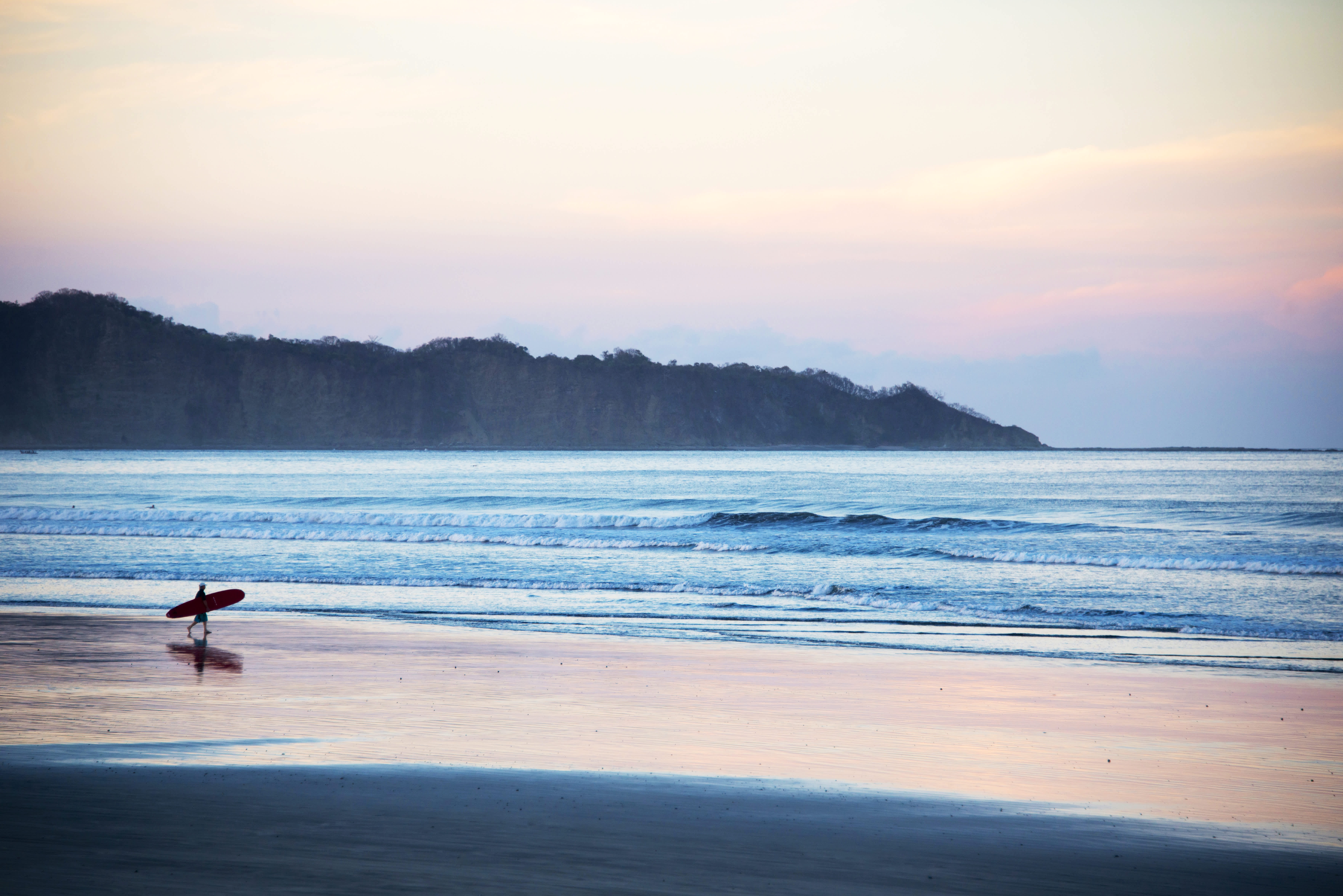 Surfer walking along the beach at sunset in Costa Rica.