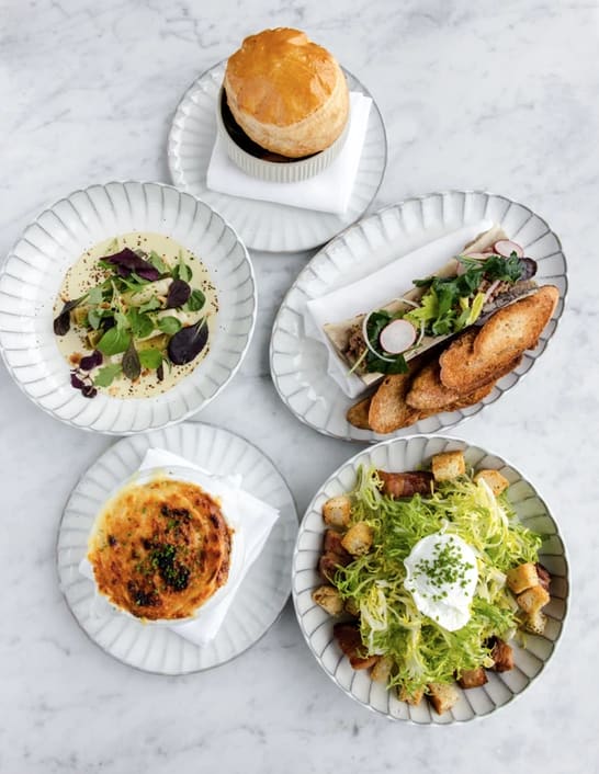 Assorted cuisine dishes presented on white patterned plates, set on a marble table at Enchante Bistro in Hampton Bays.