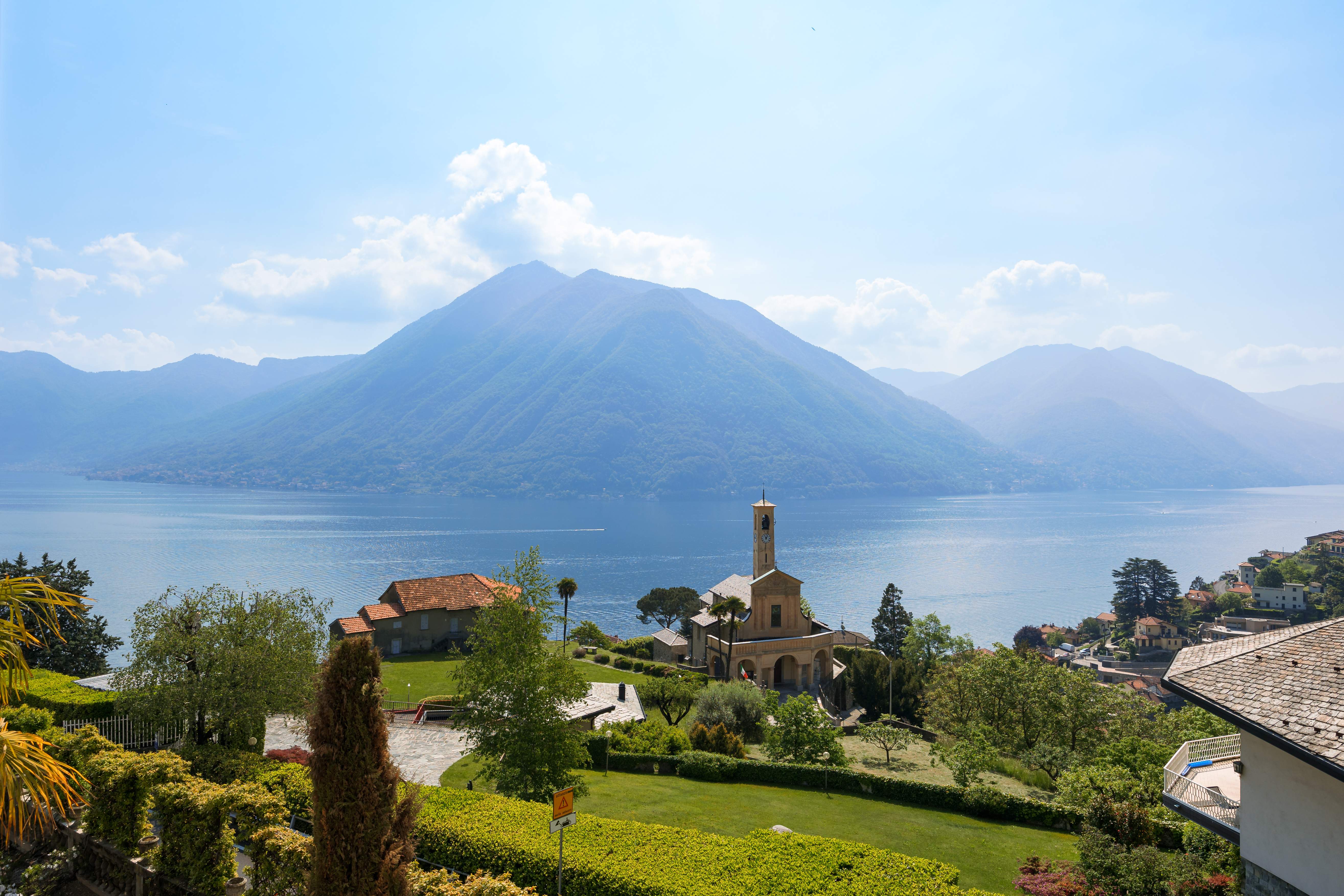 View from Exclusive Resorts' villa in Lake Como, Italy, featuring a picturesque church, lush greenery, and the serene lake surrounded by mountains.