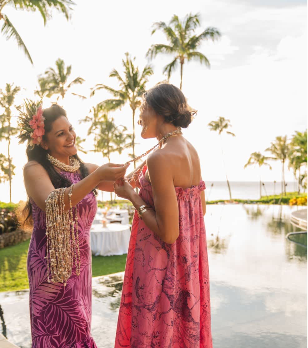 Two women exchanging leis by the poolside on the Kohala Coast.