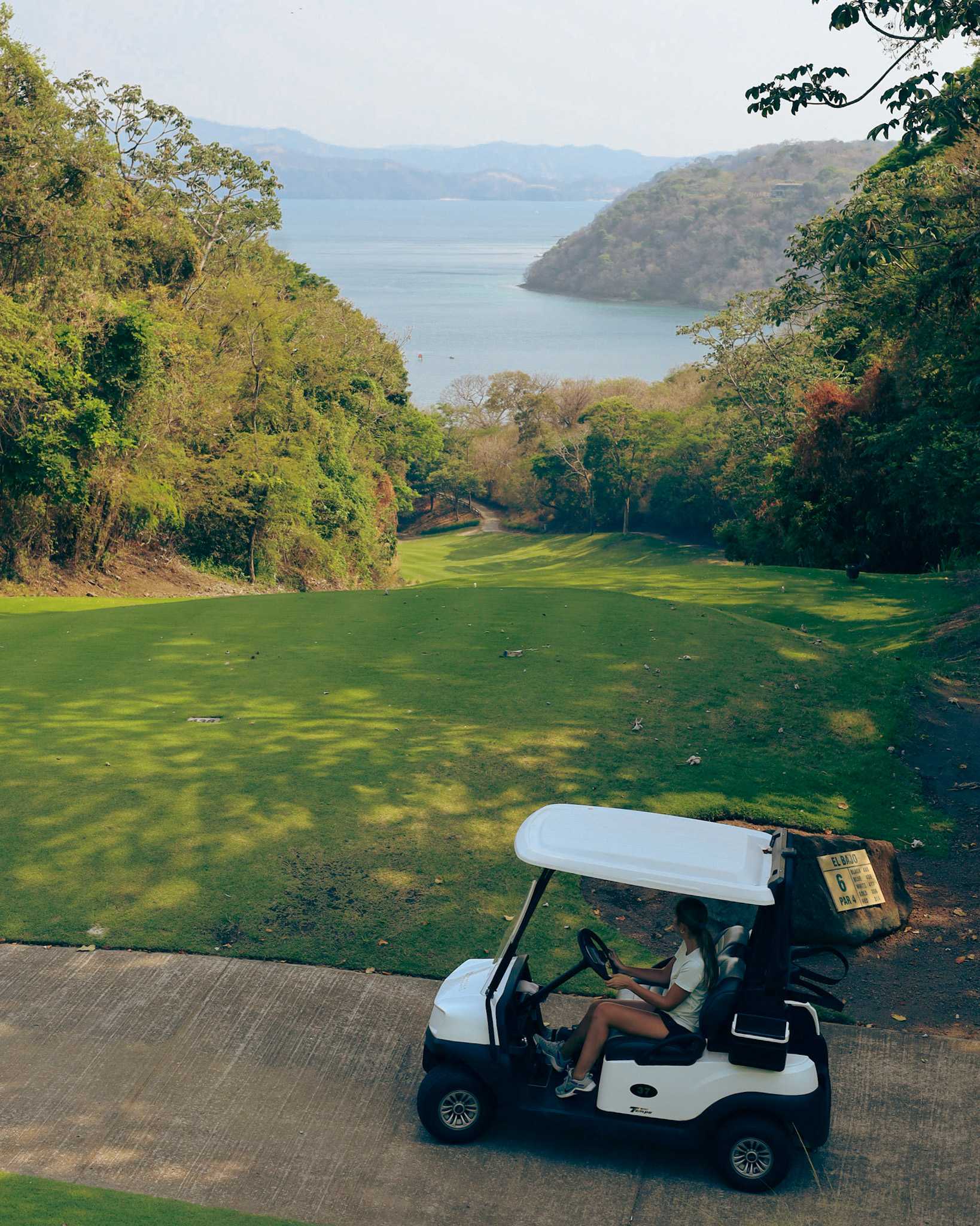 Woman driving a golf cart on a scenic golf course overlooking the ocean in Costa Rica.