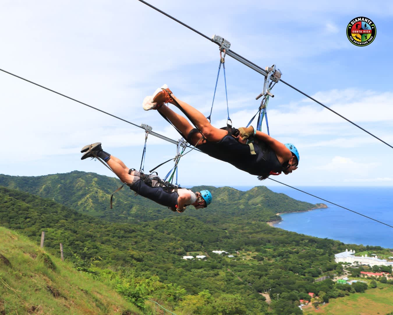 Two people ziplining over lush green hills with an ocean view in Costa Rica.