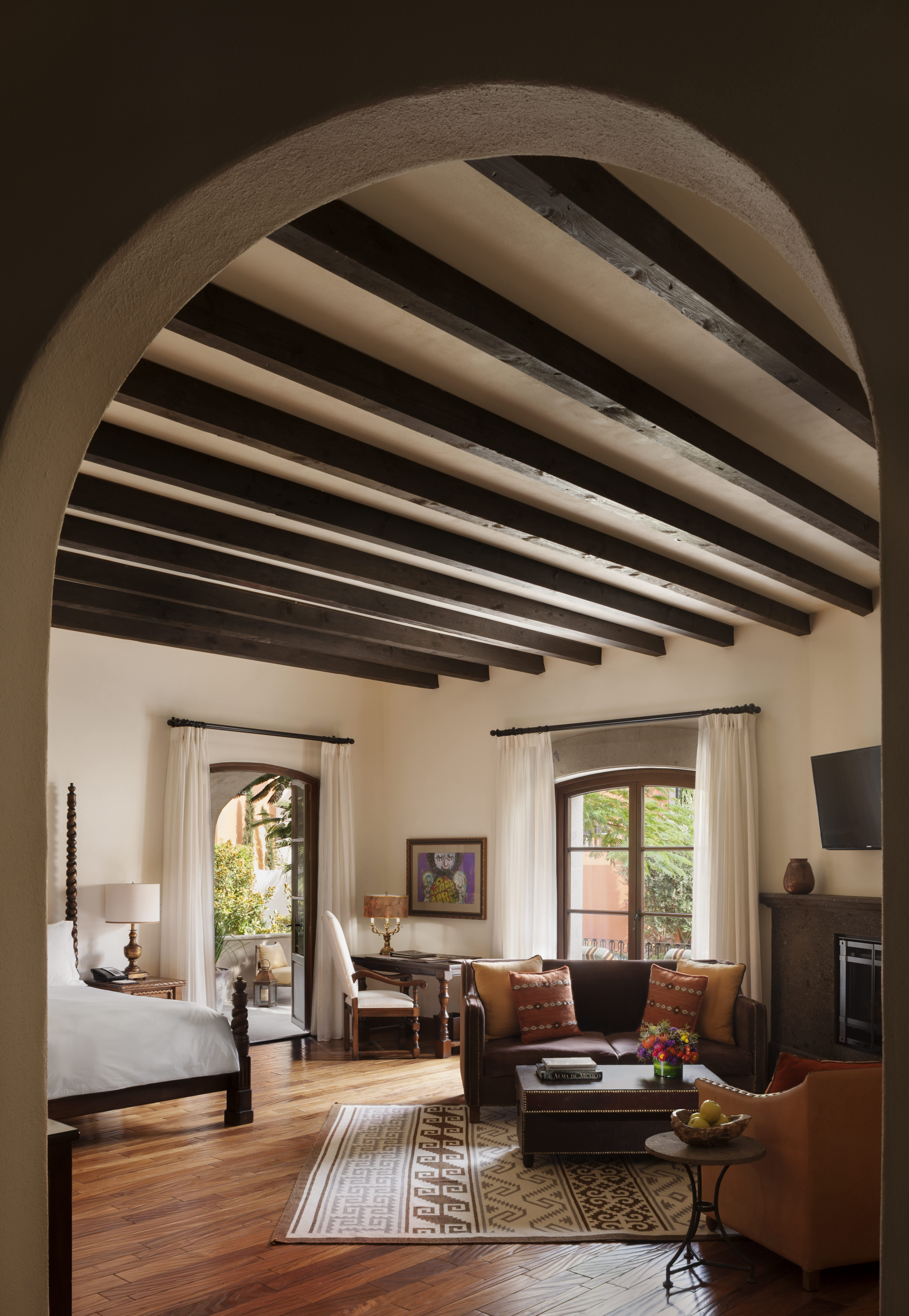 Luxury hotel room with exposed wooden beams, a cozy seating area, and a balcony view.